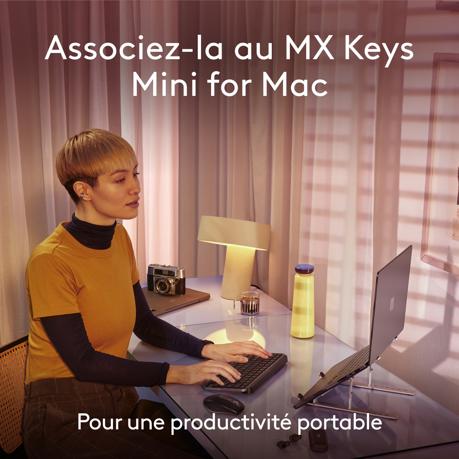 Une femme utilise un ordinateur portable et un clavier. L'ordinateur portable est sur un support. Il y a un appareil photo et une lampe sur le bureau.