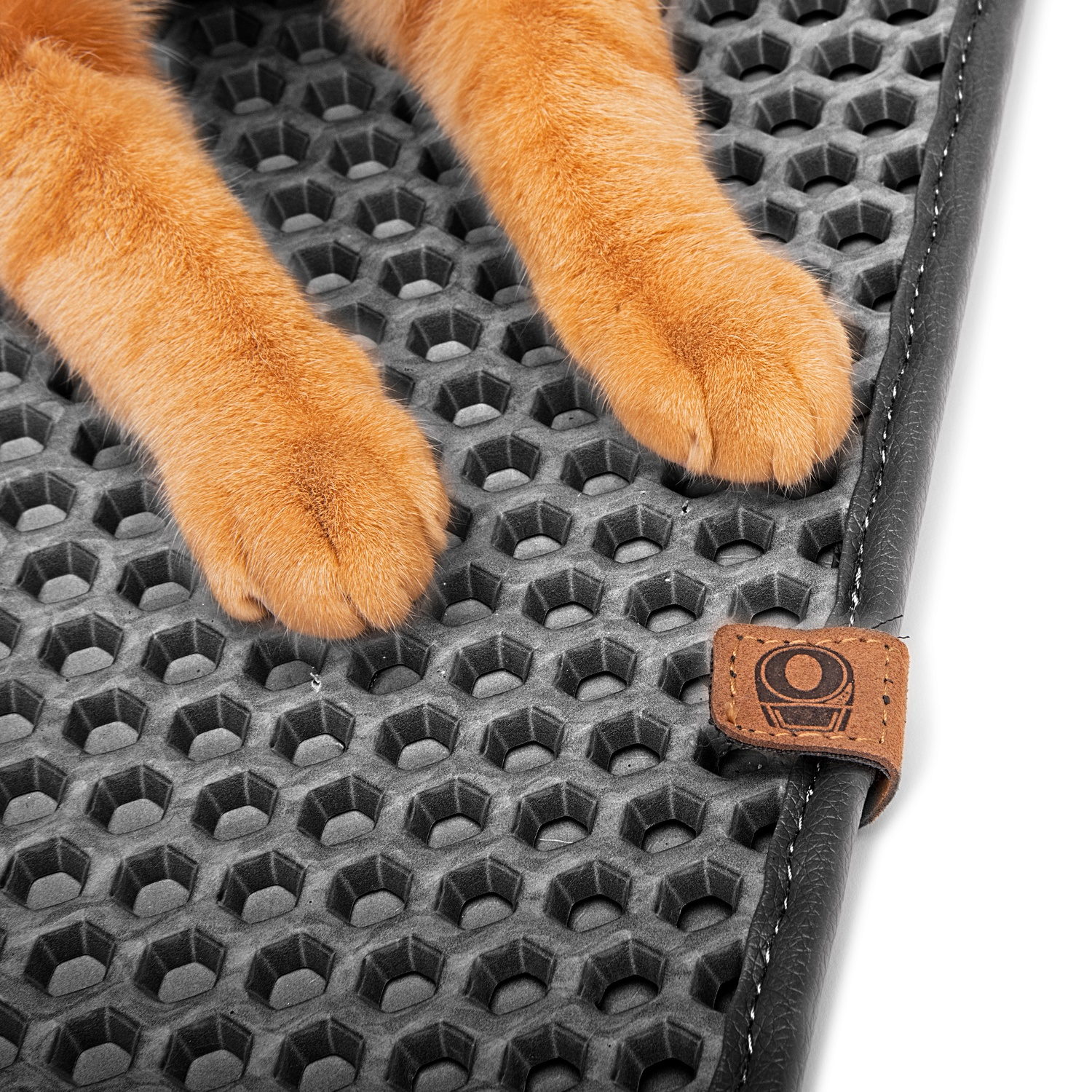 Orange cat paws on a hexagonal grey cat litter mat with a leather tag.