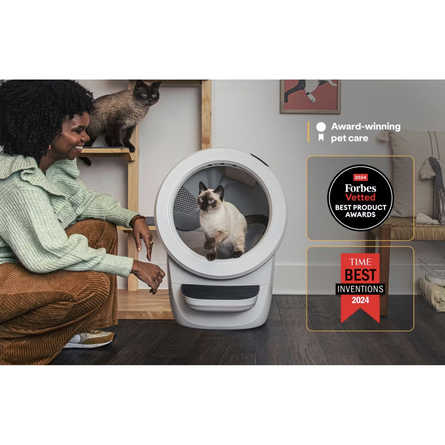 Een vrouw en twee katten die interageren met een automatische kattenbak, met awards.