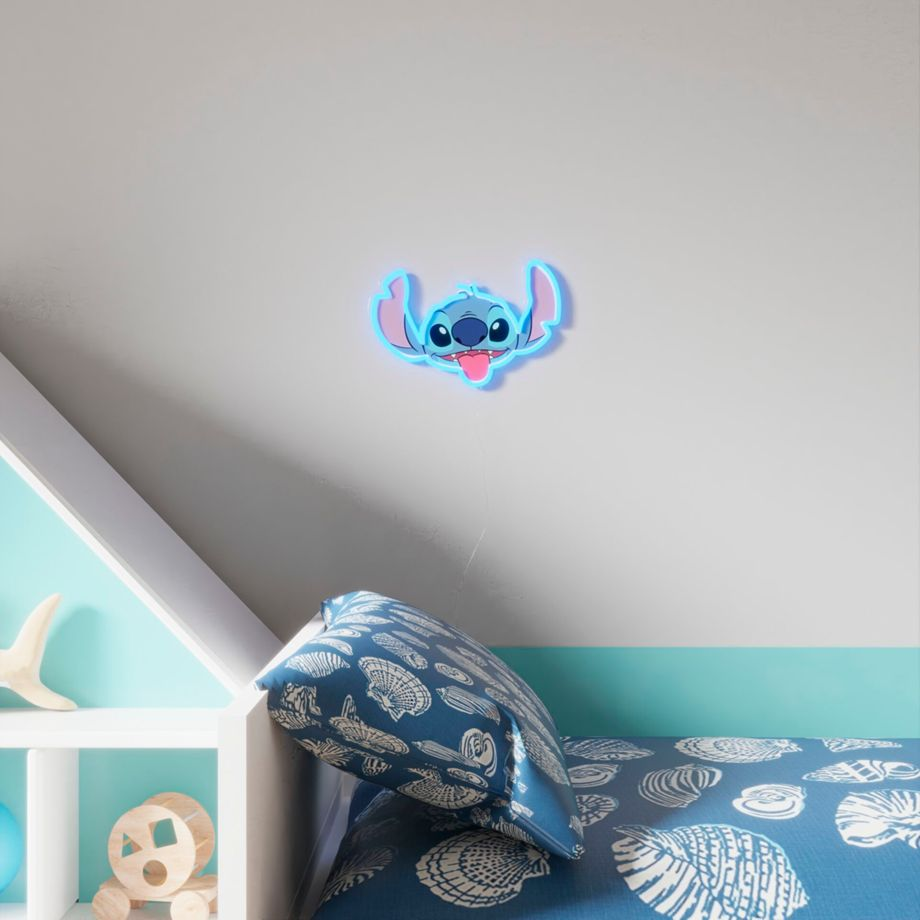 Niebieska neonowa lampa z głową Stitcha na ścianie. Poniżej łóżko z niebieską pościelą w muszelki.