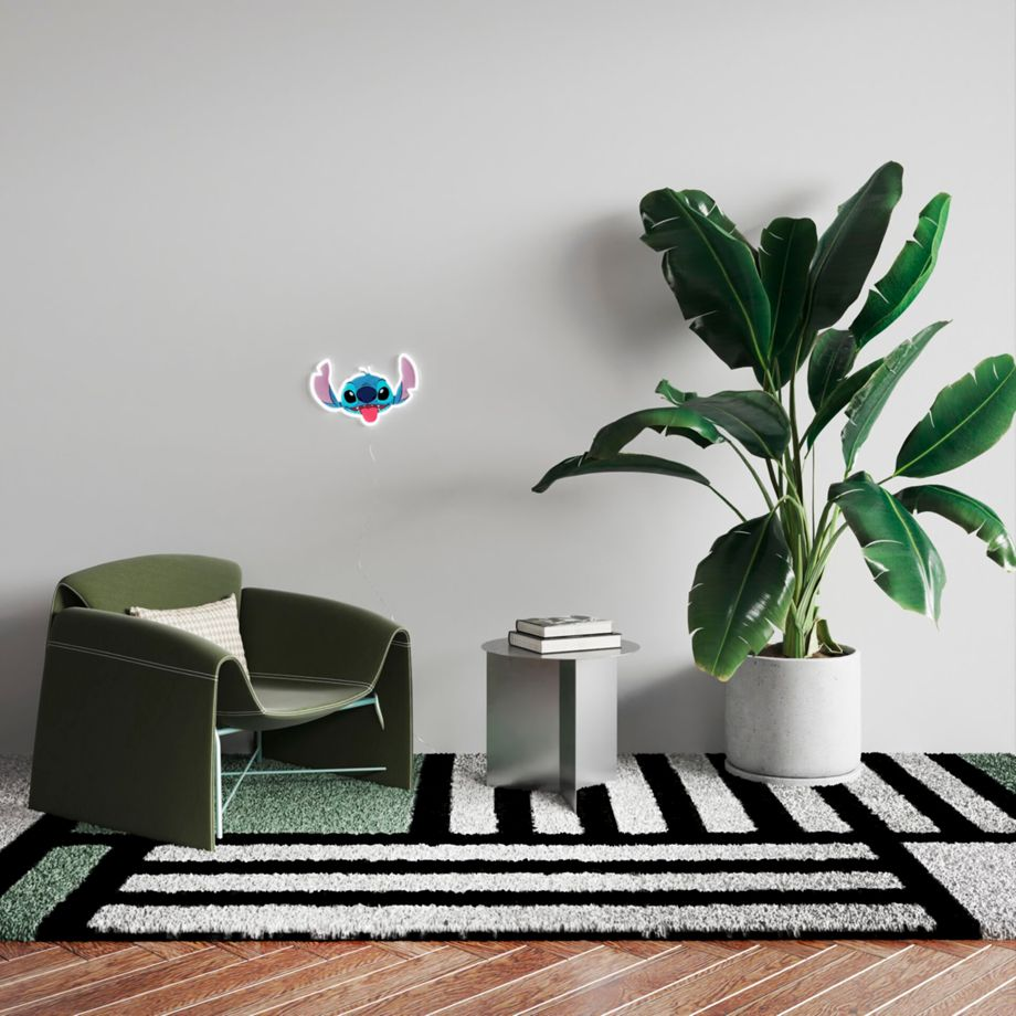 Naklejka ścienna Stitch nad zielonym krzesłem i pasiastym dywanem.