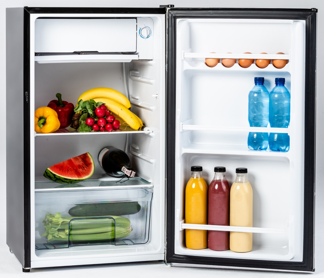 Otwarta lodówka wypełniona produktami spożywczymi, owocami, napojami i jajkami.