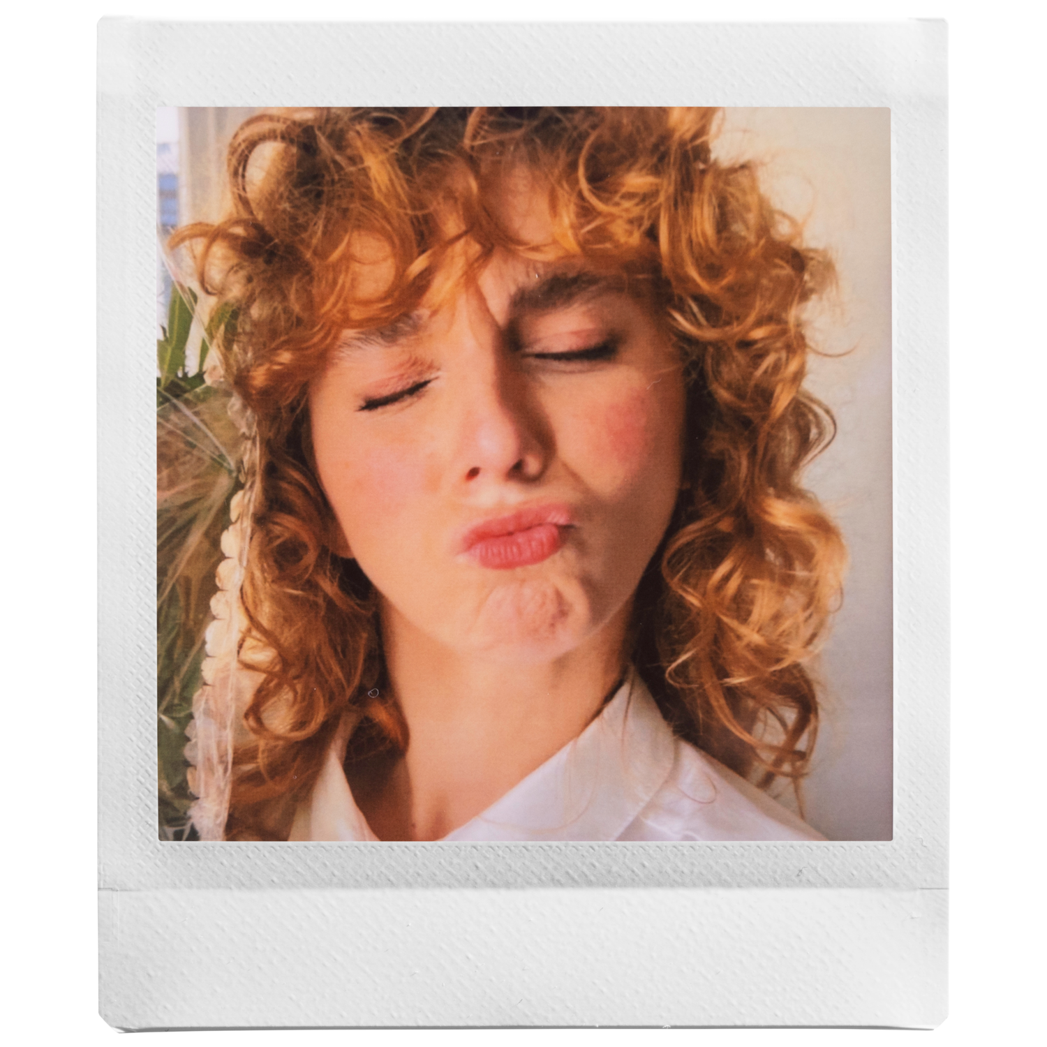 Photo de style Polaroid d'une femme aux cheveux roux bouclés, les yeux fermés, faisant une moue de baiser.