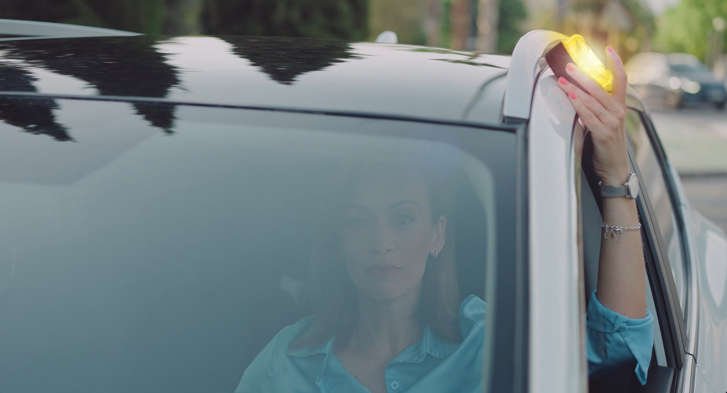 Mujer en el coche enciende una luz de advertencia. Coches y casas en el fondo.