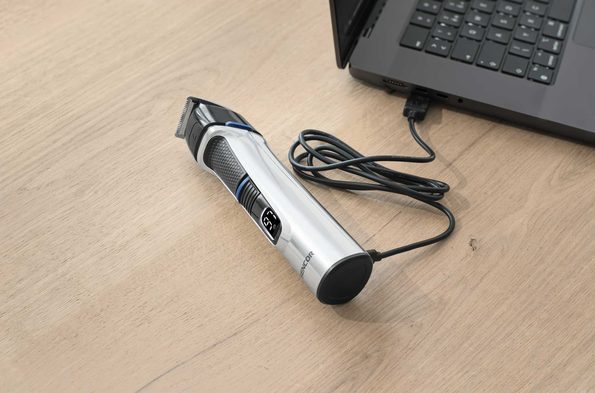 Ezüst elektromos hajvágó, USB-n keresztül laptophoz csatlakoztatva.