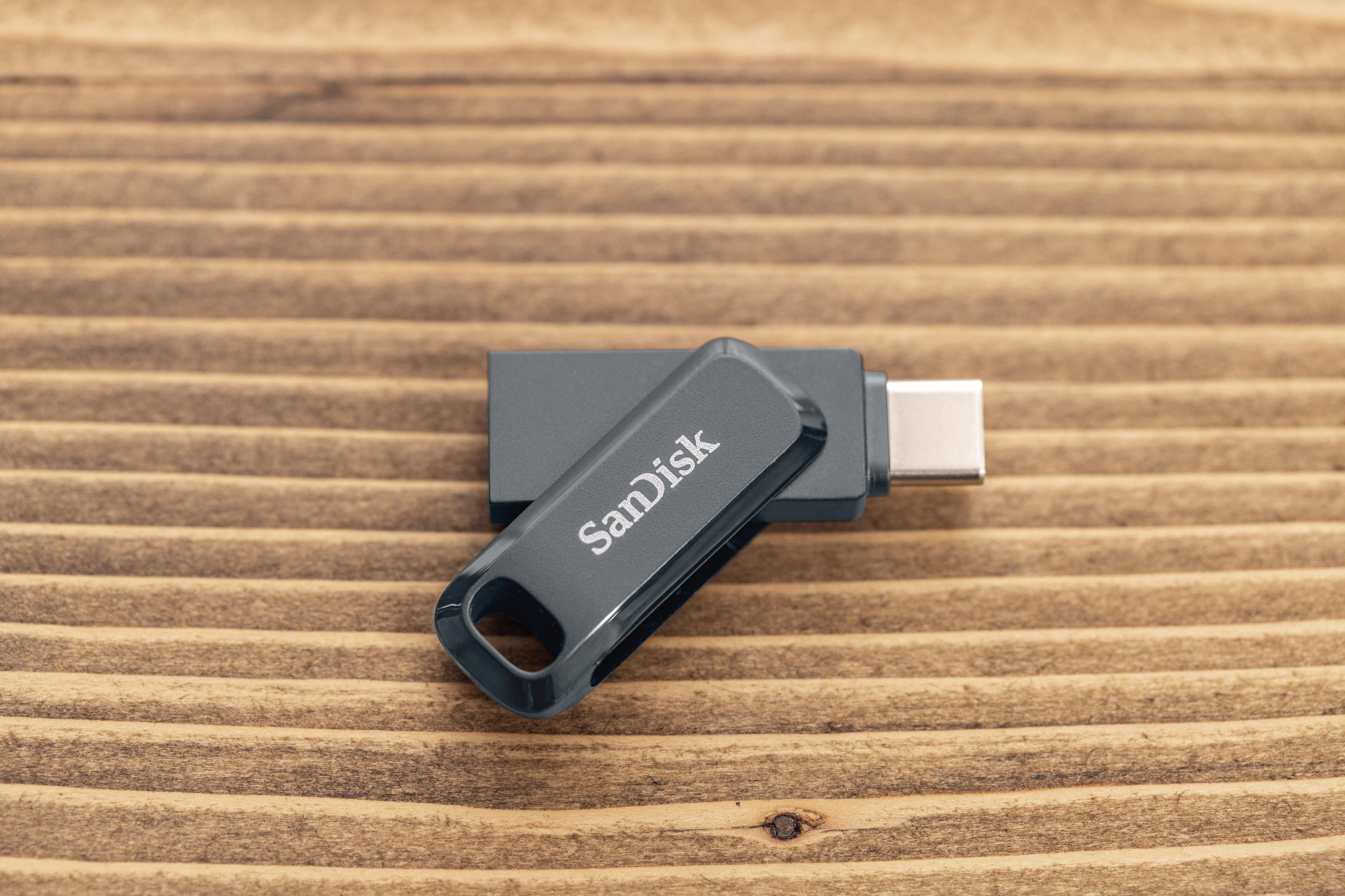 Grauer SanDisk USB-Stick mit silbernem Stecker liegt auf einer gestreiften Holzoberfläche.