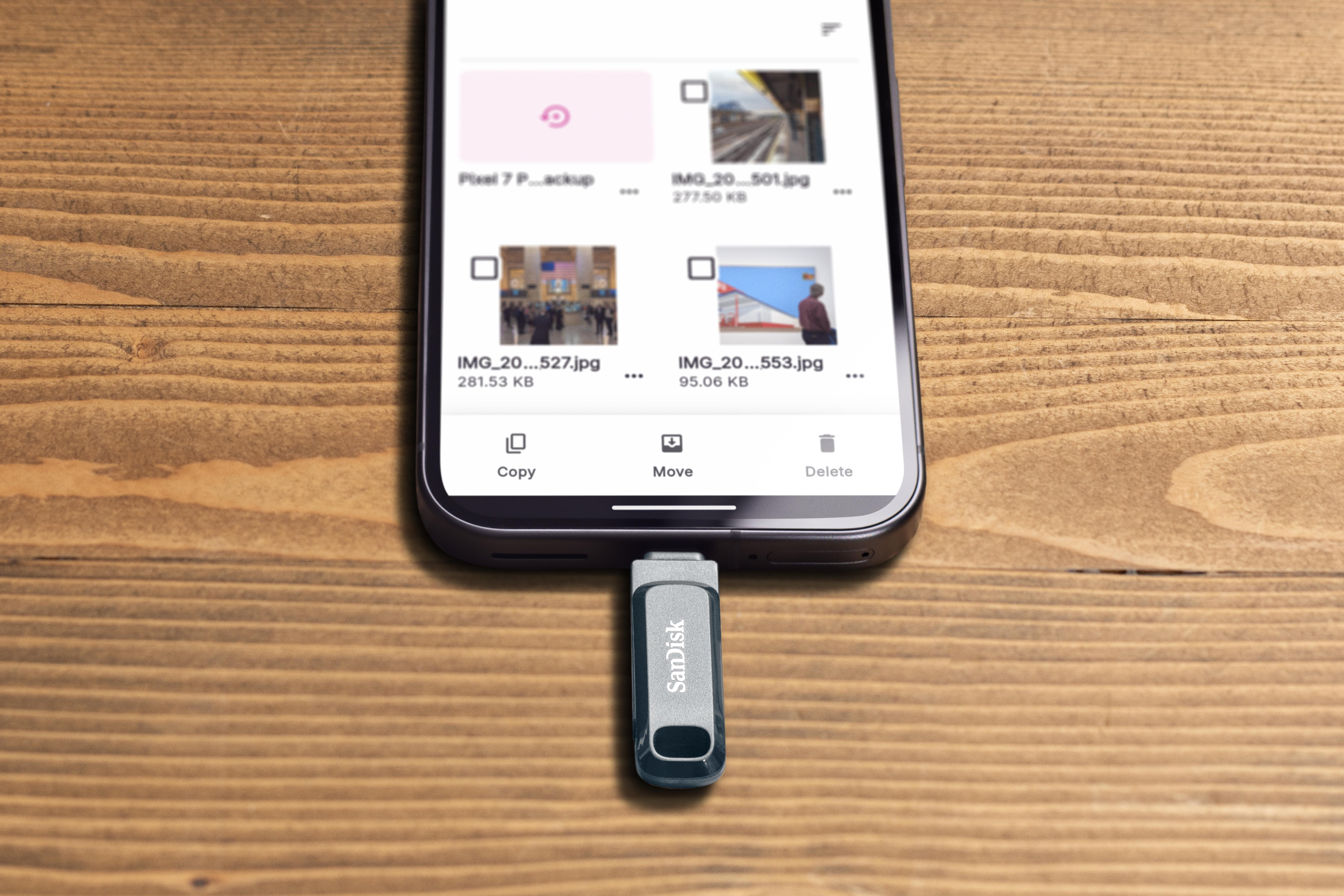 Ein Telefon mit Dateisymbolen ist mit einem SanDisk USB-Laufwerk auf einer Holzoberfläche verbunden.