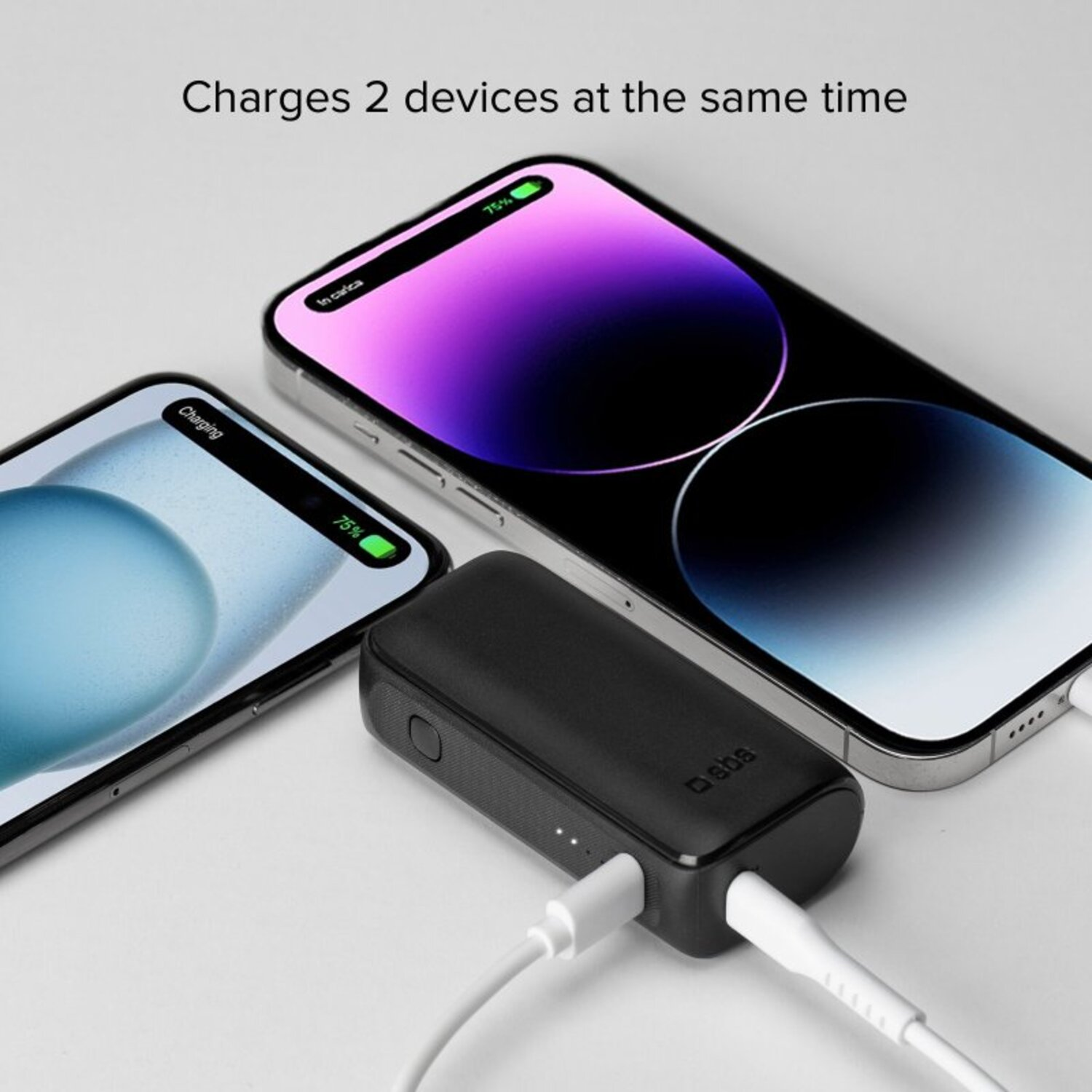 Batterie externe noire chargeant deux téléphones. Câbles de charge blancs, fond clair.