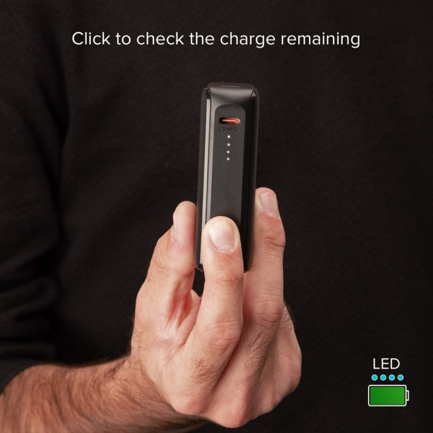 Une main tenant un chargeur portable noir avec un indicateur de batterie vert.