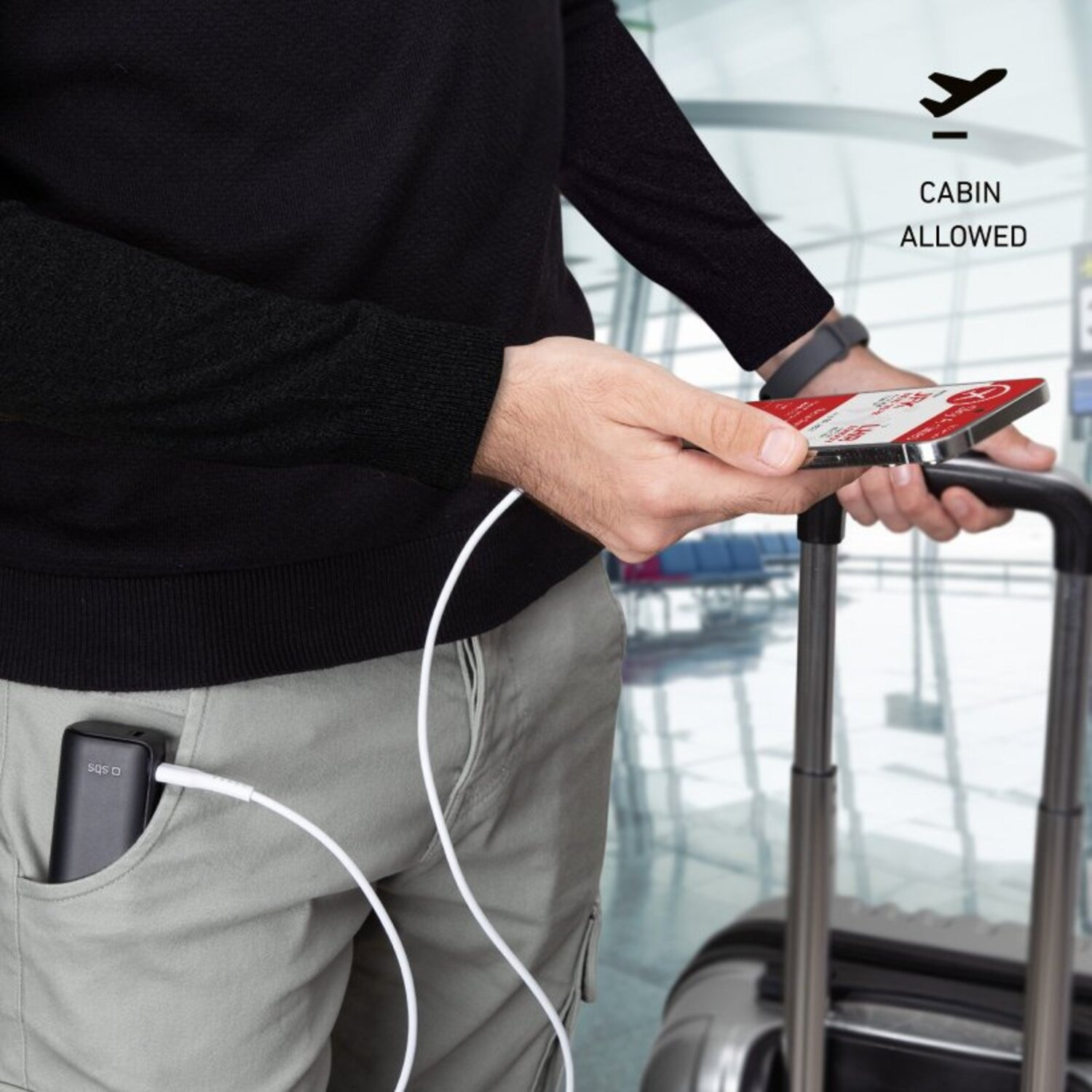 Une personne en chemise noire et pantalon kaki tient un téléphone qui charge depuis une batterie externe dans sa poche.