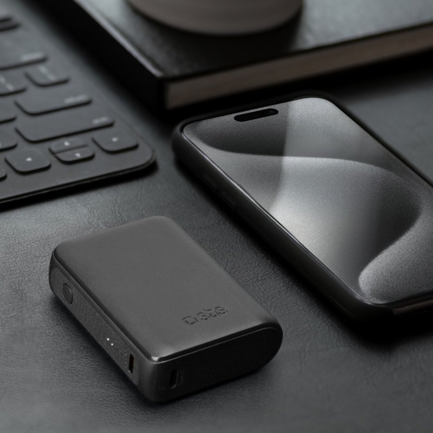Accessoires noirs sur une surface noire: une batterie externe, un téléphone et un clavier.
