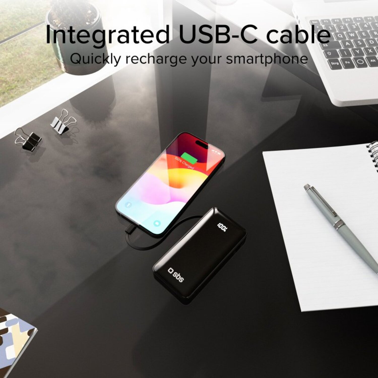 Batterie externe noire chargeant un téléphone sur un bureau avec un stylo et du papier.