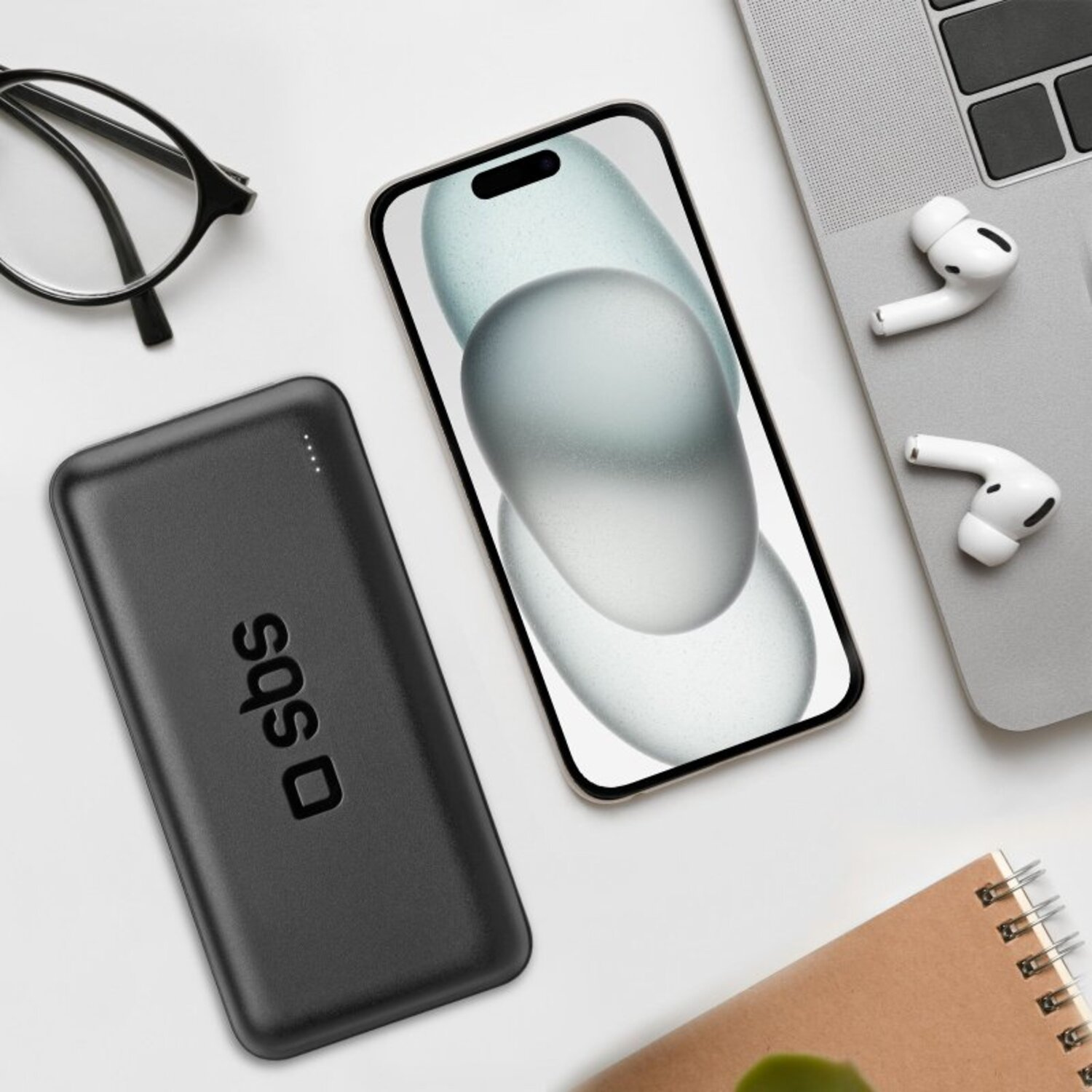 A black power bank, phone, earbuds, and notebook on a white surface.