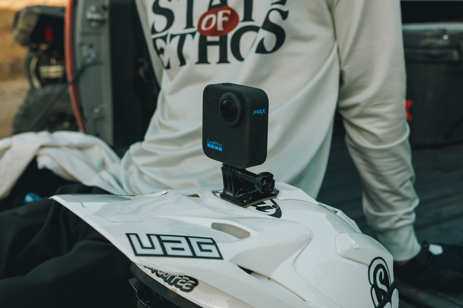 Cámara GoPro Max montada en un casco blanco. Hombre en el fondo usando una camisa.