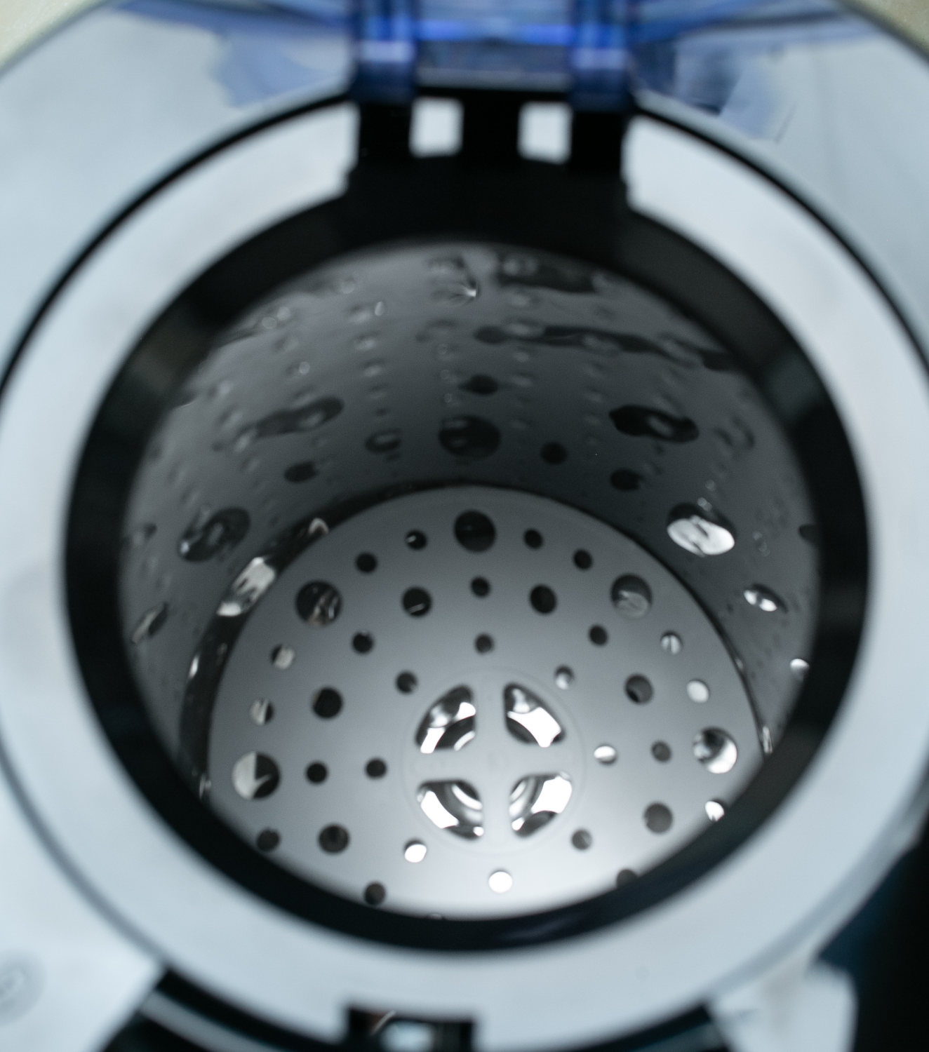 Wewnątrz bębna pralki, z otworami, oświetlonego od góry, widoczne krople wody.