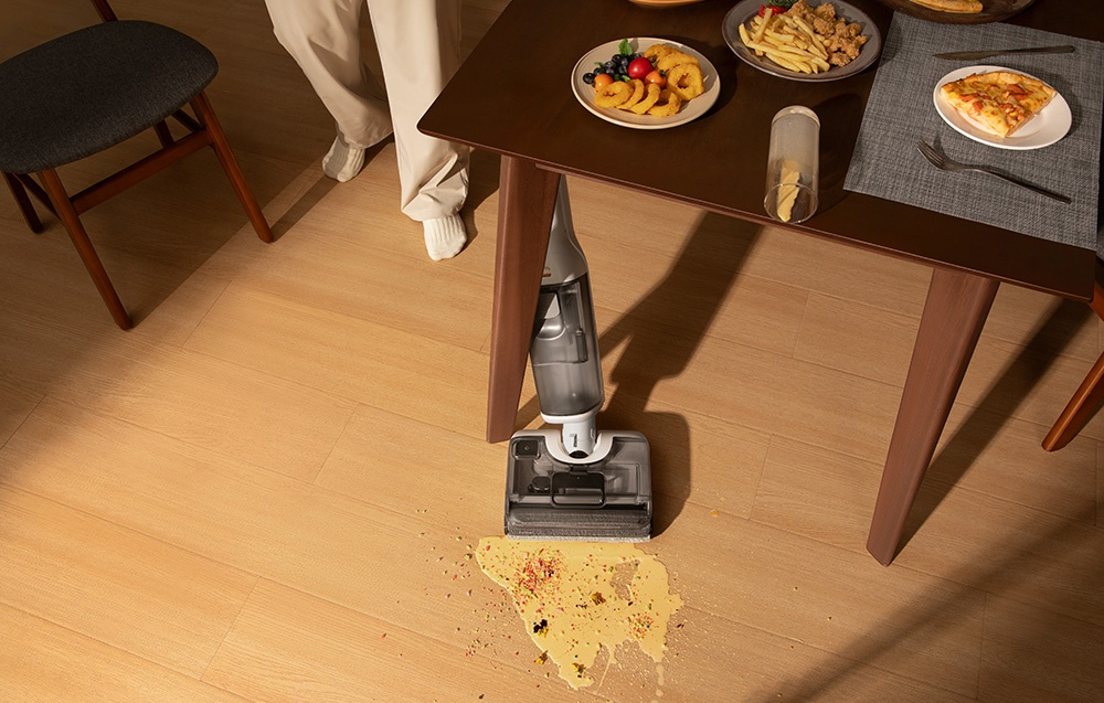Odkurzacz do podłóg stoi na drewnianej podłodze z rozlanym jedzeniem wokół niego.