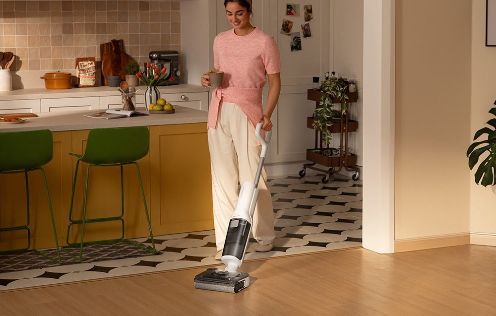 Kobieta używająca białego odkurzacza na drewnianej podłodze.