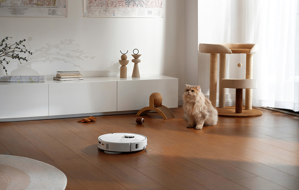 Pokój z białym odkurzaczem automatycznym na drewnianej podłodze, kotem, drapakiem, meblami.