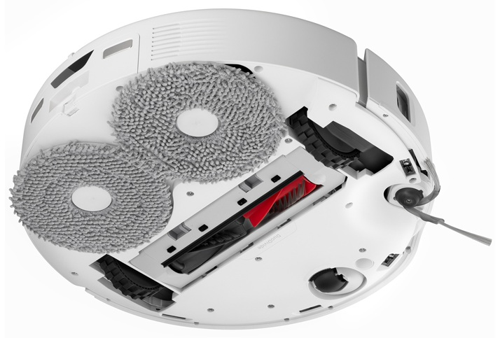 Odkurzacz automatyczny, widok od spodu. Okrągły kształt, widoczne szczotki i koła. Białe tło.