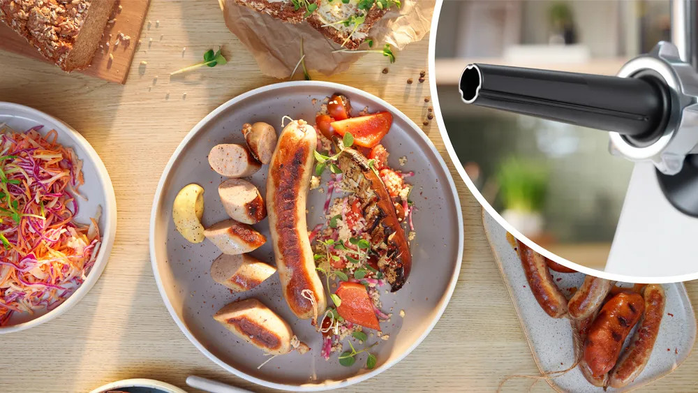 Zdjęcie z góry talerza z grillowanymi kiełbaskami, warzywami i chlebem. Obok maszynka do mięsa.