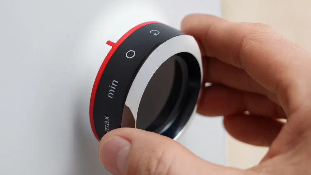 Zbliżenie dłoni obracającej pokrętło z czerwonymi i czarnymi akcentami na białej powierzchni.