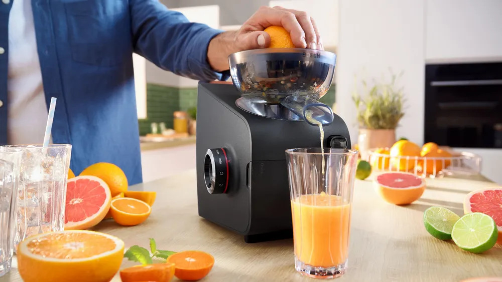 Osoba wyciska pomarańczę w wyciskarce.