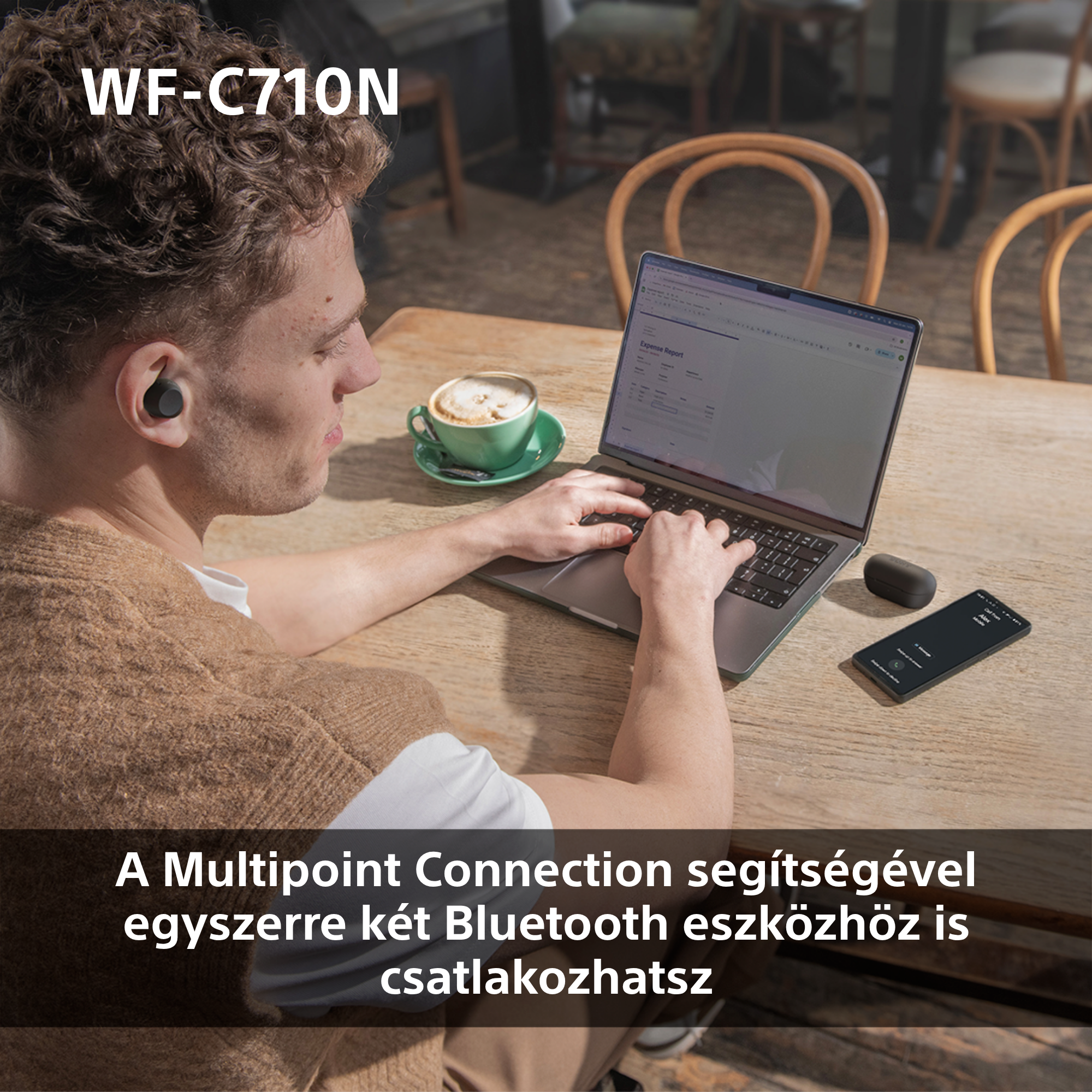 Egy férfi fejhallgatóval laptopot használ egy faasztalon kávéval és telefonnal.