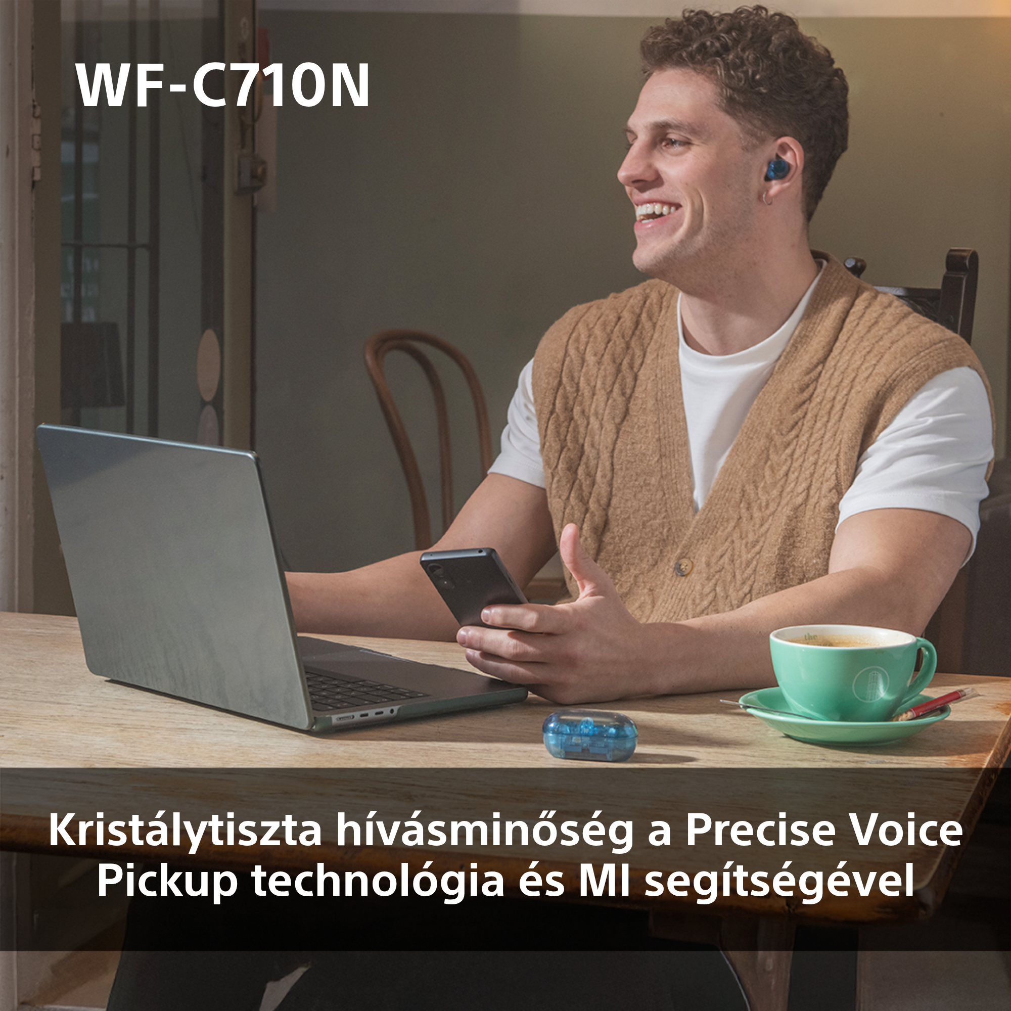 Egy mosolygó férfi kék fülhallgatóval, laptopot használ. Egy kávéscsésze és egy kis kék hangszóró.