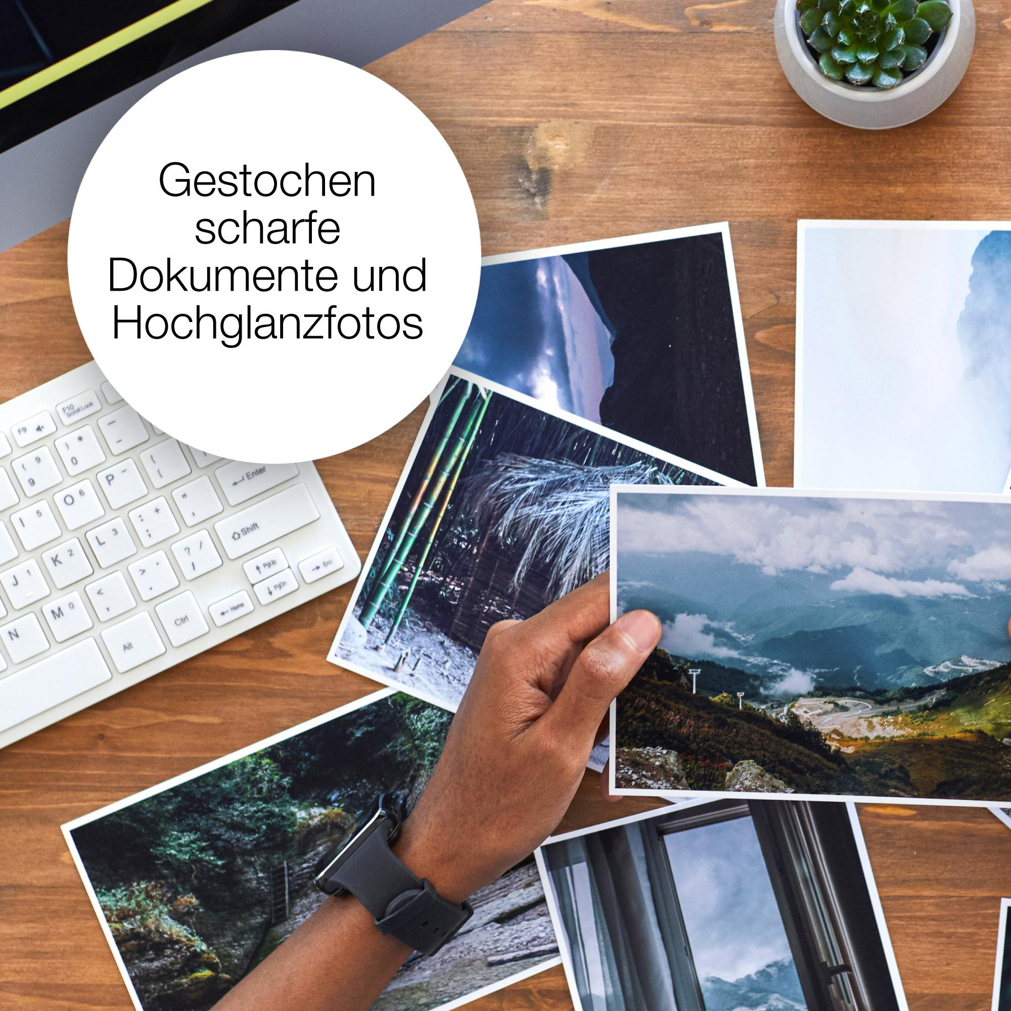 Hand hält Fotos auf einem Holztisch, Tastatur und Pflanze im Hintergrund, mit Textüberlagerung.
