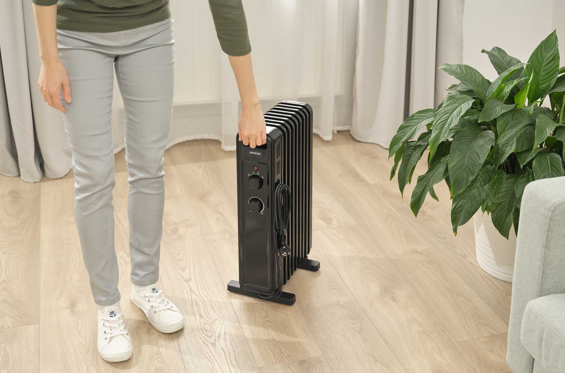 Személy fekete olajradiátort tart. Fekete fűtőtest és világos fa padló.