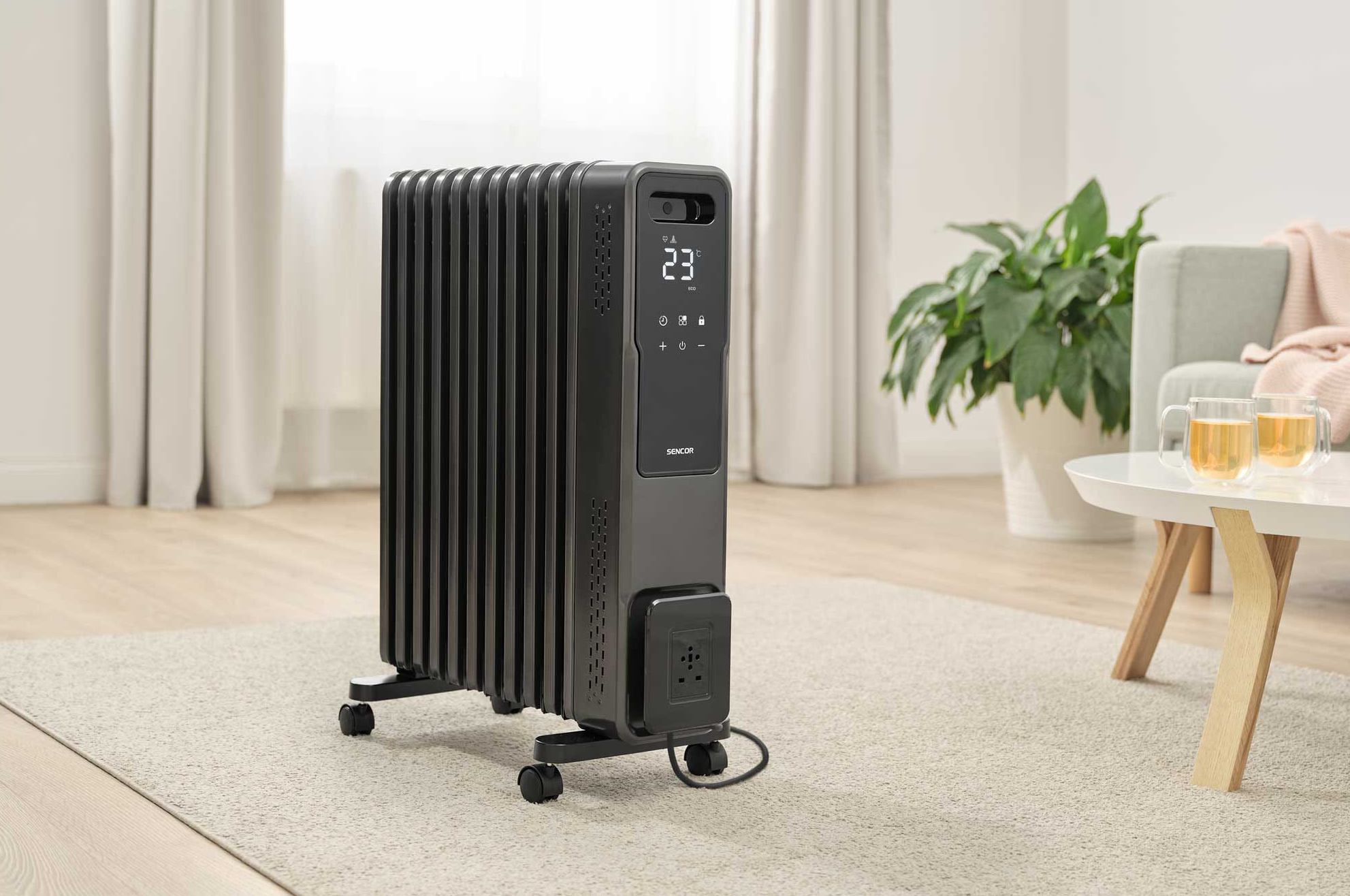 Fekete elektromos hősugárzó kerekeken, nappaliban, növénnyel, asztallal, ablakkal.