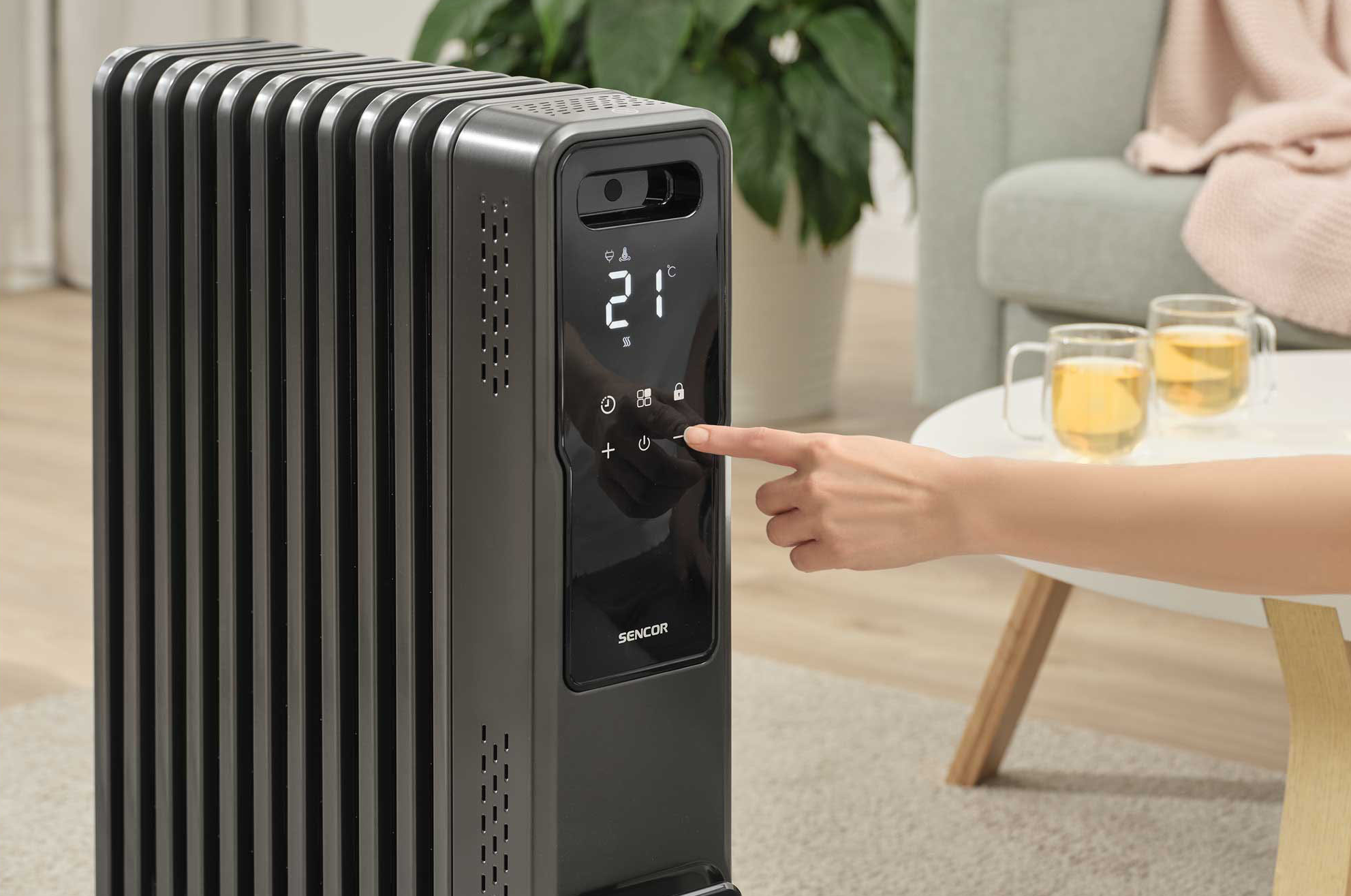Egy kéz megnyom egy gombot egy sötétszürke fűtőpanelen, beállítva a hőmérsékletet.