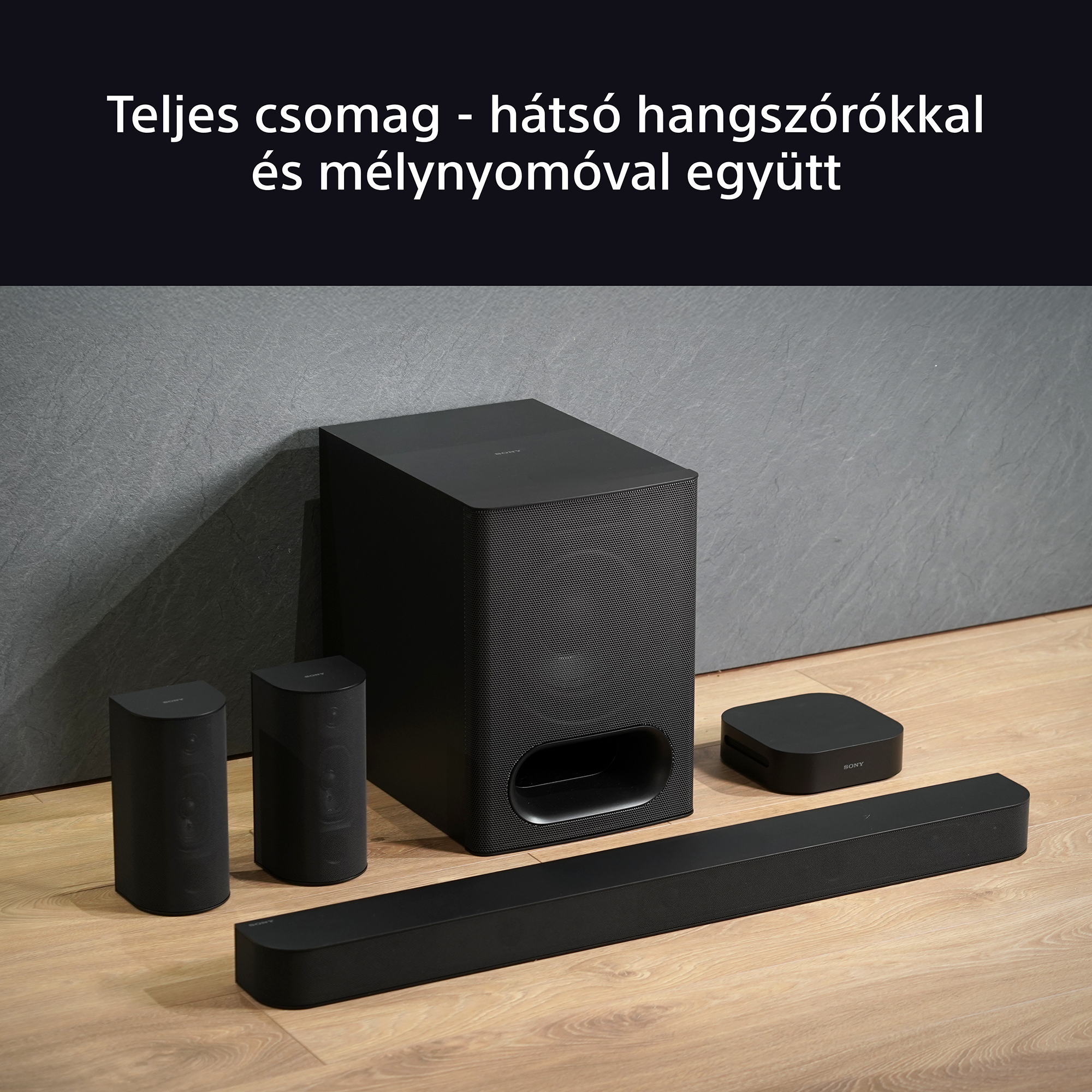Egy fekete soundbar, két hangszóró és egy mélynyomó látható egy szobában. Fekete háttér.