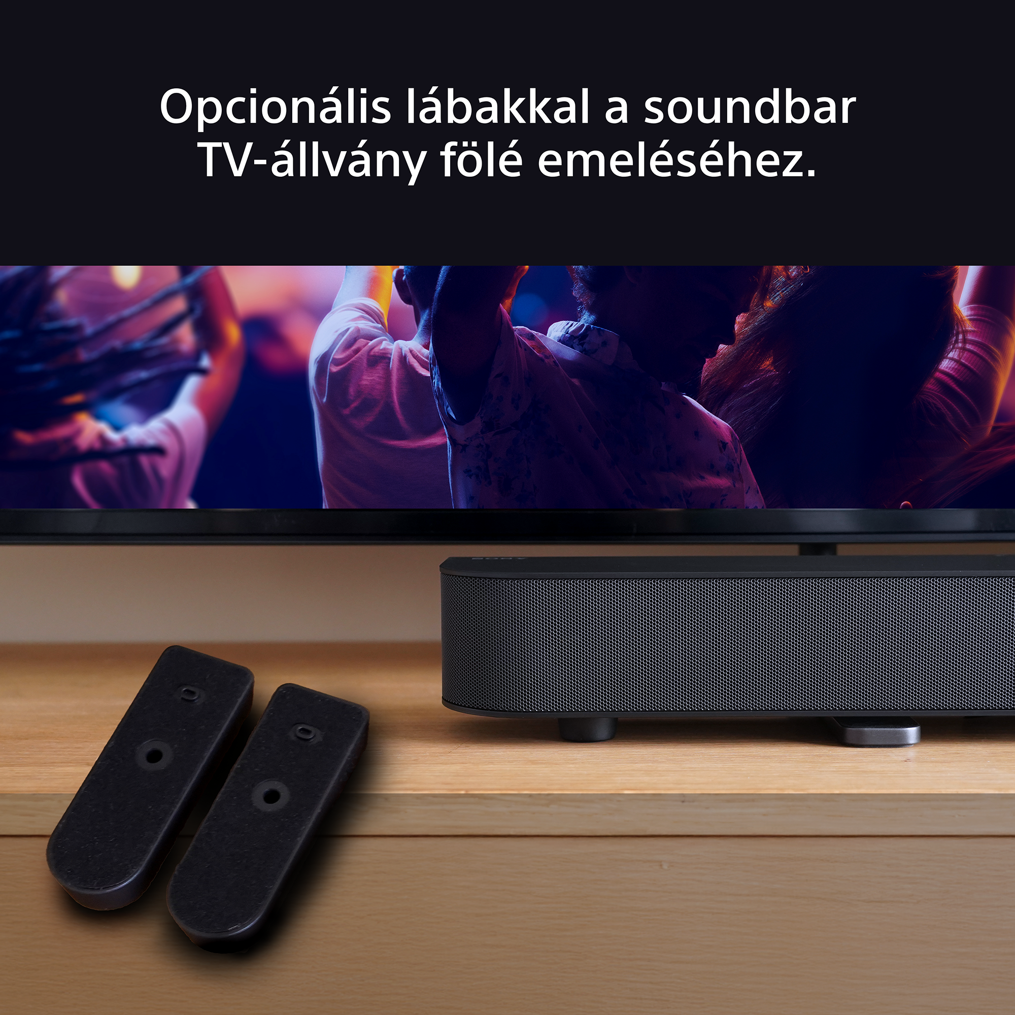 A soundbar egy fa felületre van helyezve. Két fekete távirányító van előtte. A háttér elmosódott.