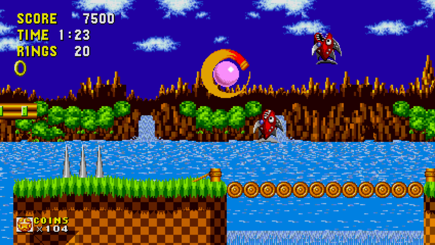 Scena di un videogioco retrò. Sonic corre su un ponte sull'acqua. Nemici e monete visibili.