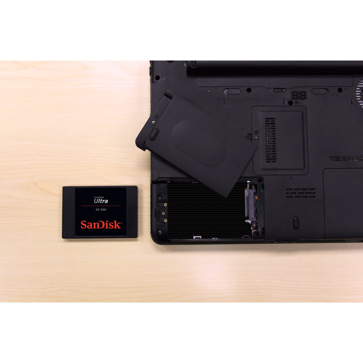 Ordenador portátil con la tapa de la batería abierta, junto a un SSD SanDisk.