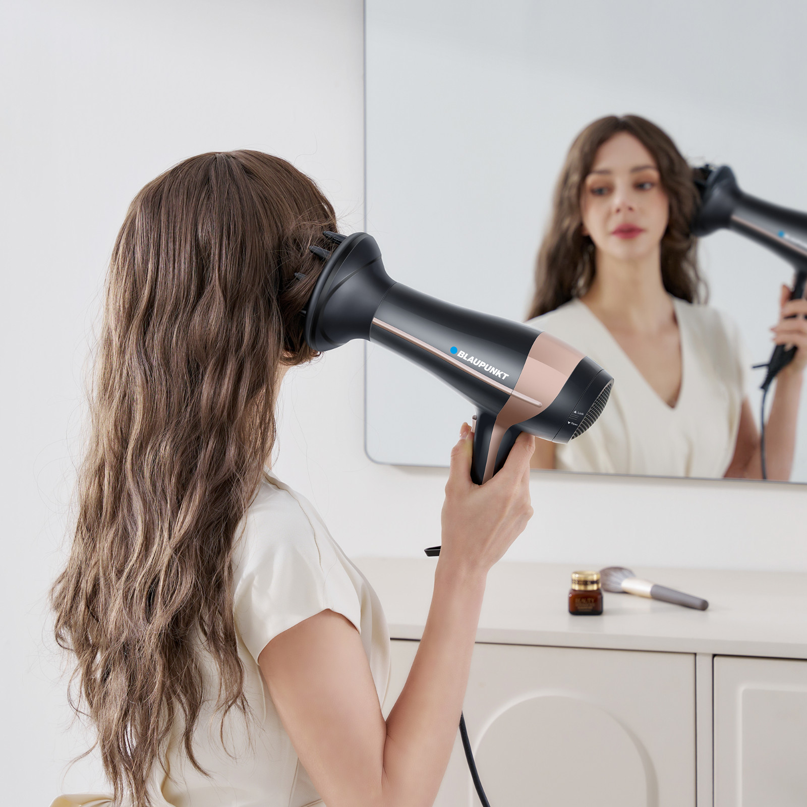 Kobieta używa suszarki do włosów przed lustrem. Suszarka z napisem BLAUPUNKT.
