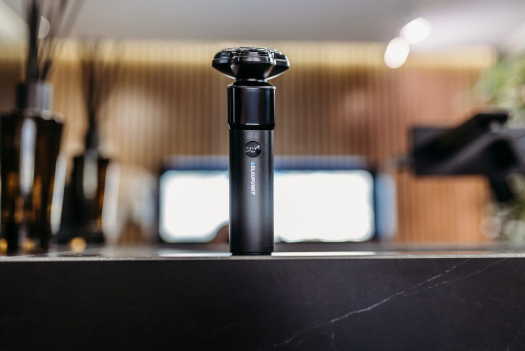 Czarna golarka elektryczna na blacie. Tło ukazuje rozmyte wnętrze z elementami dekoracyjnymi.