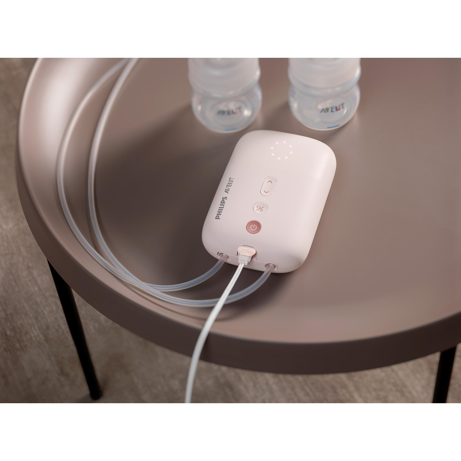 Een witte Philips Avent borstkolf met slangen en flessen op een bruine tafel.