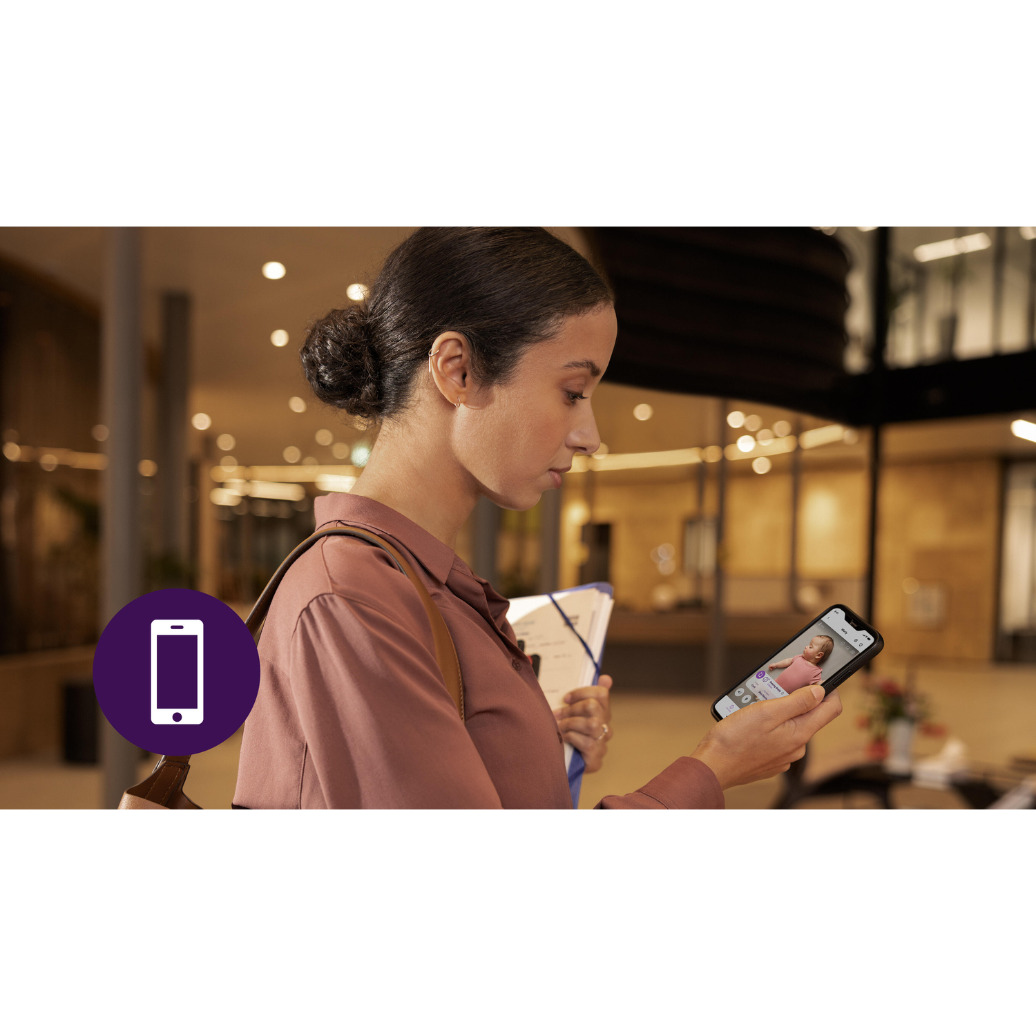 Vrouw kijkt naar telefoon, toont babyfoon-app. In een gebouw.