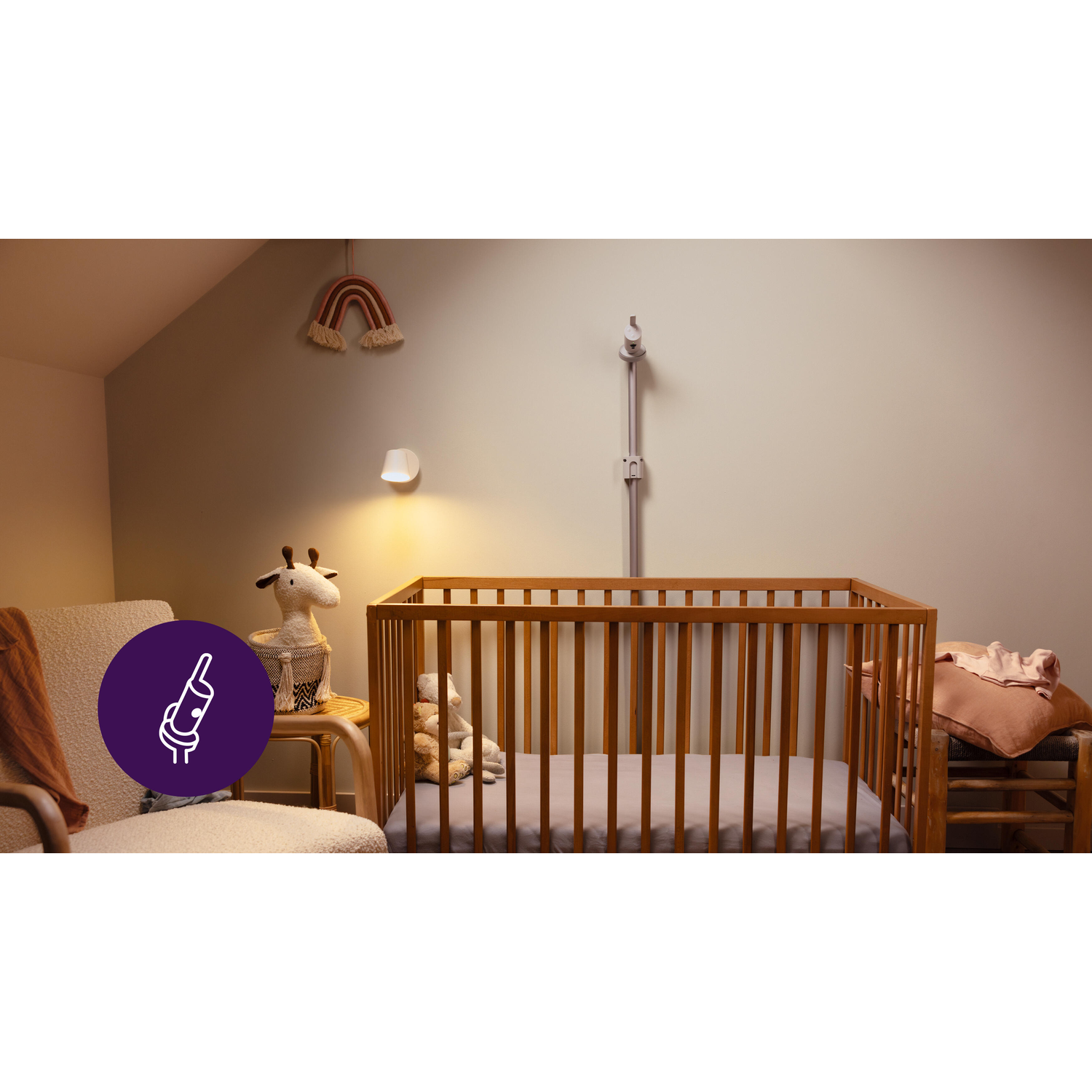 Een babyfoonopstelling in een kinderkamer. Een wieg, een wandlamp en een regenboogdecoratie.