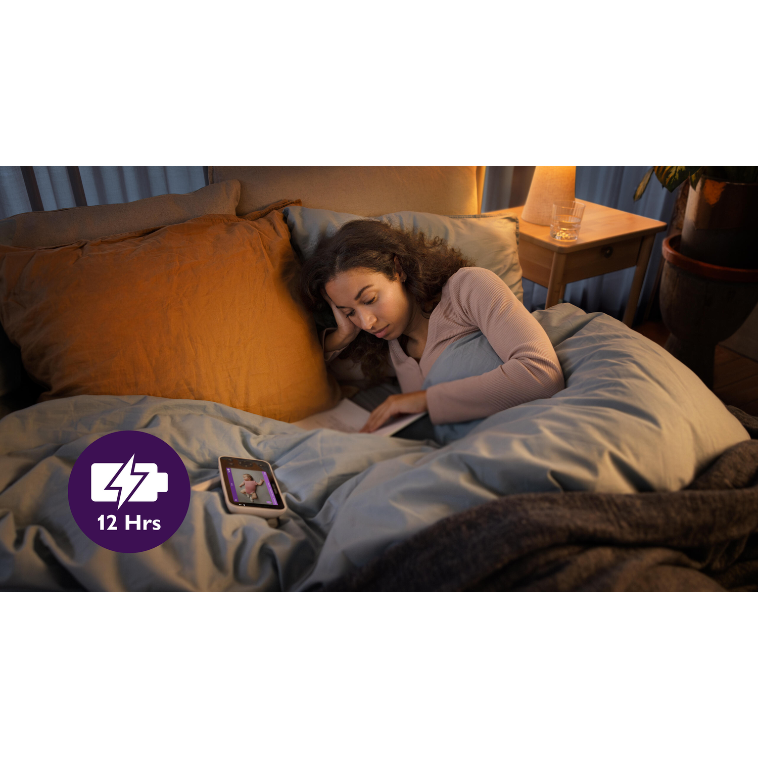 Een vrouw in bed, leest een boek op een telefoon. De telefoon toont een video. Donkere kamer.