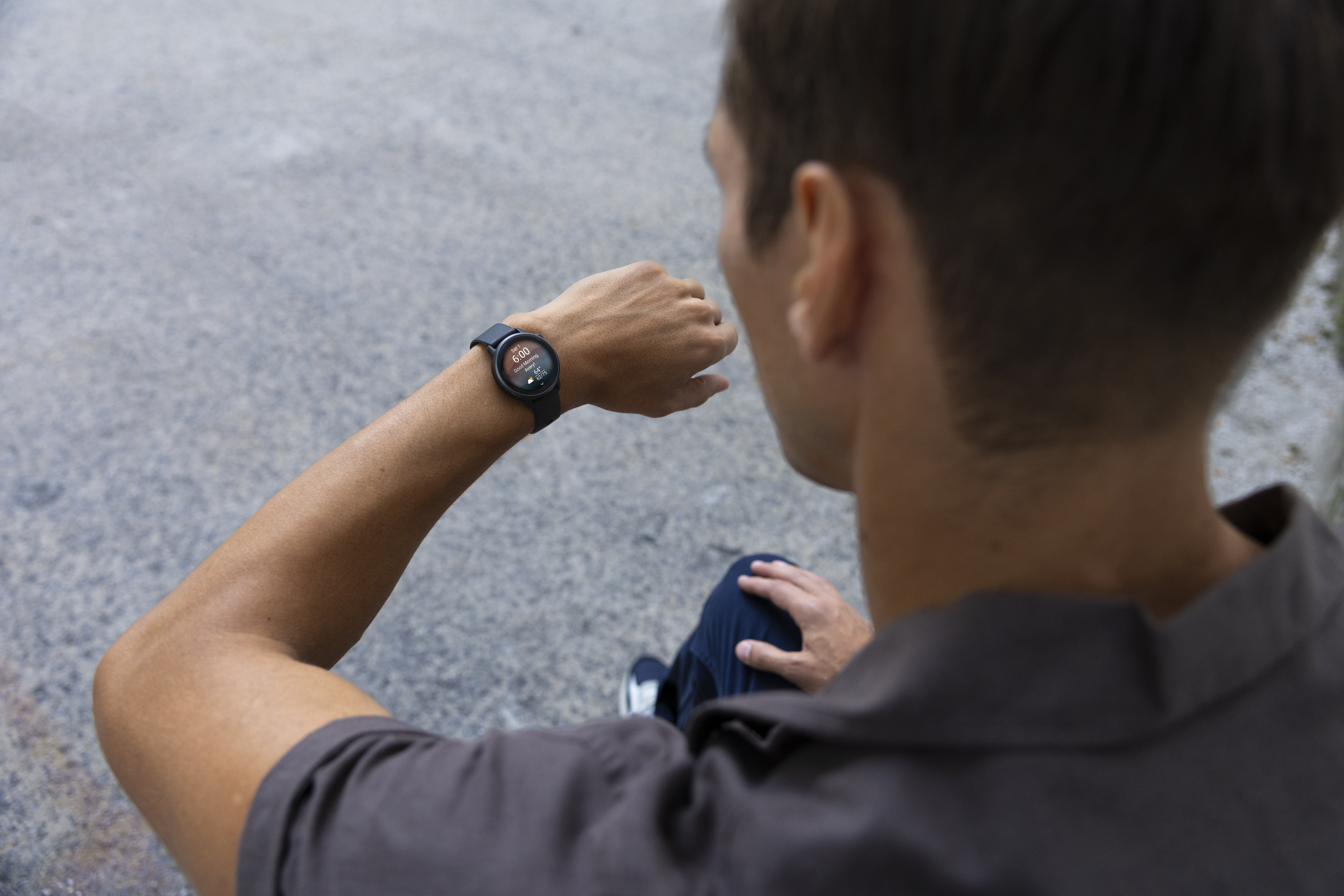 Ein Mann betrachtet eine schwarze Smartwatch an seinem Handgelenk. Draußen, Asphalt.