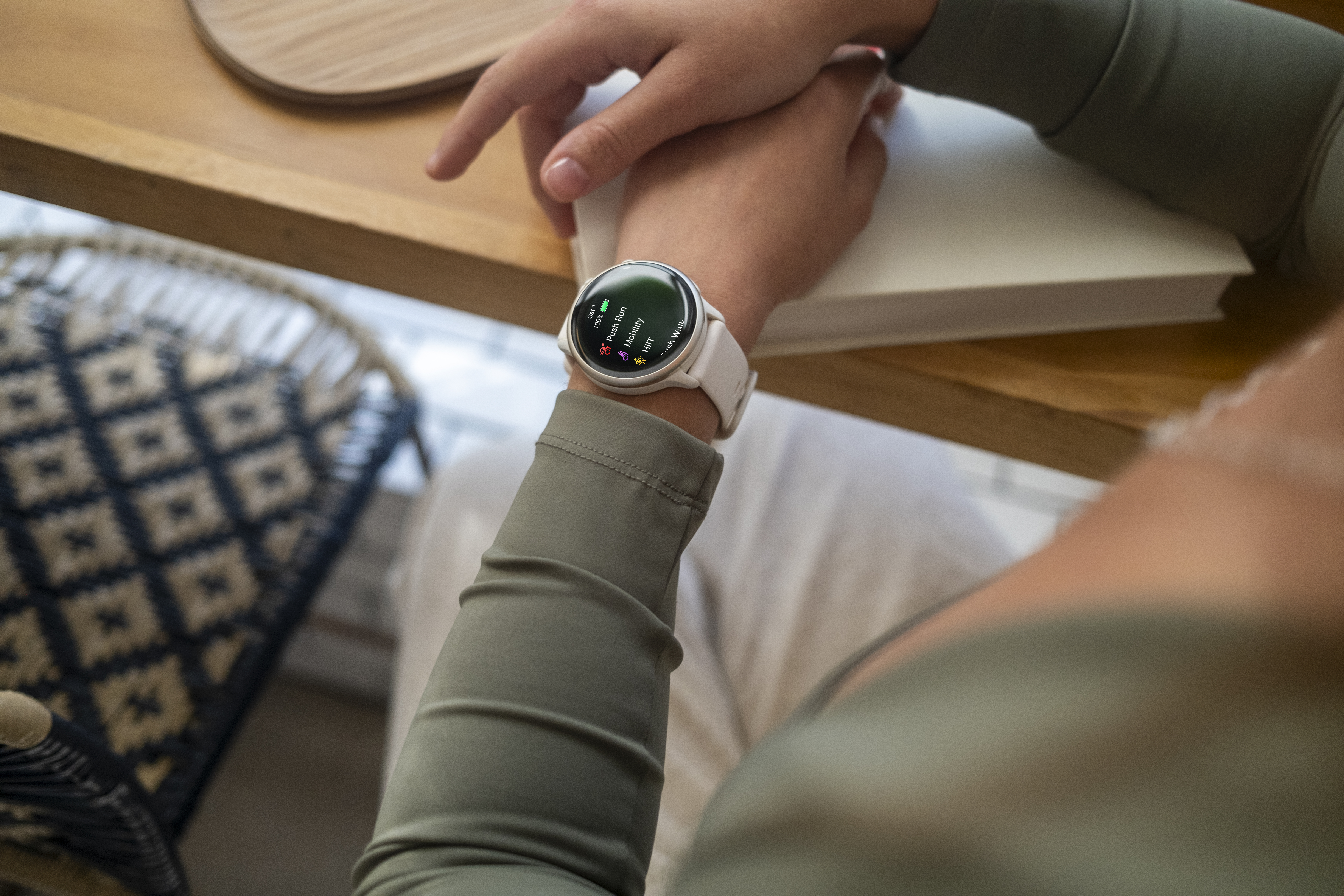 Person trägt Smartwatch, sitzt an Tisch mit Buch. Die Uhr ist weiß.