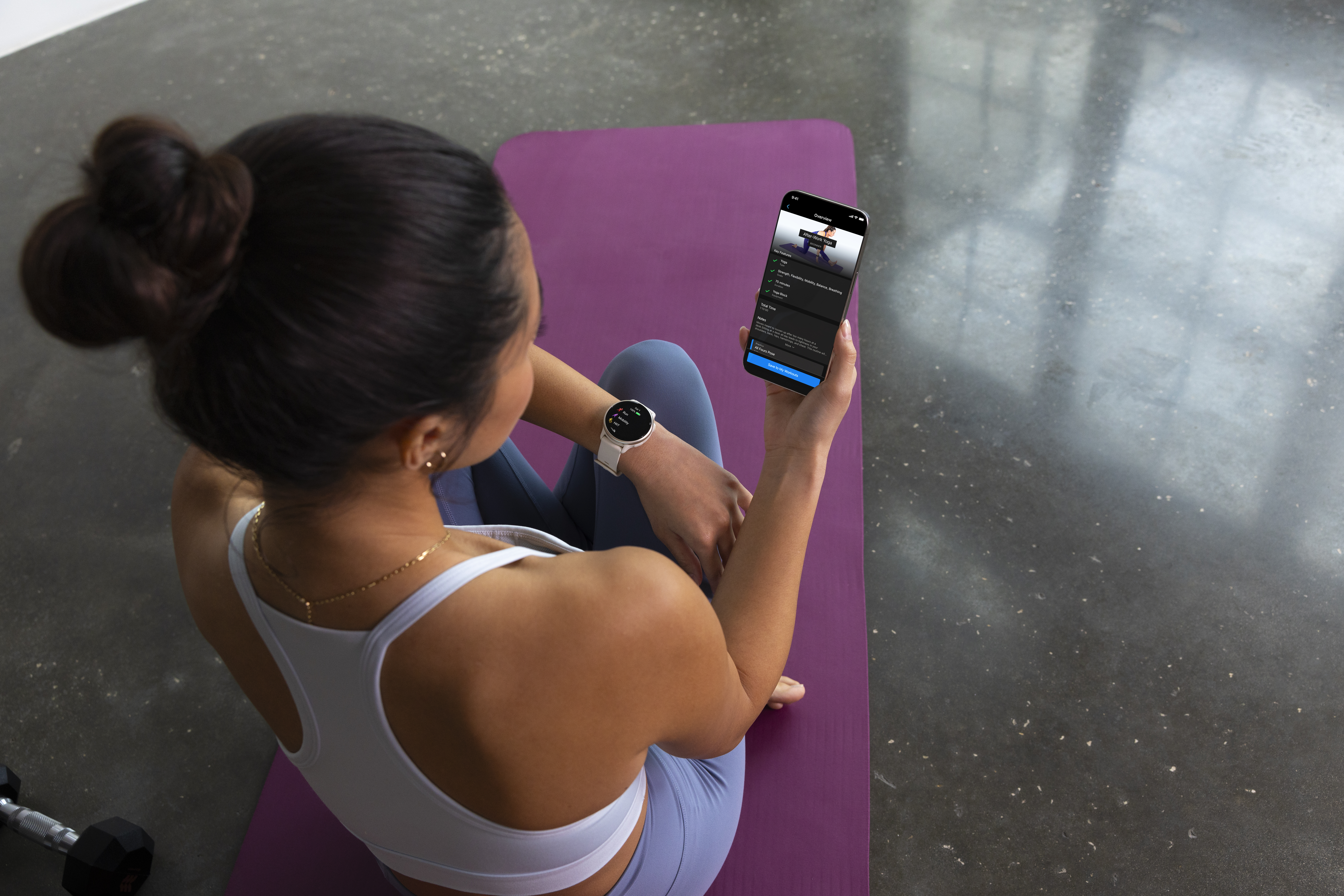 Eine Frau sitzt auf einer Yogamatte und schaut auf ihr Telefon, das eine Workout-App anzeigt.