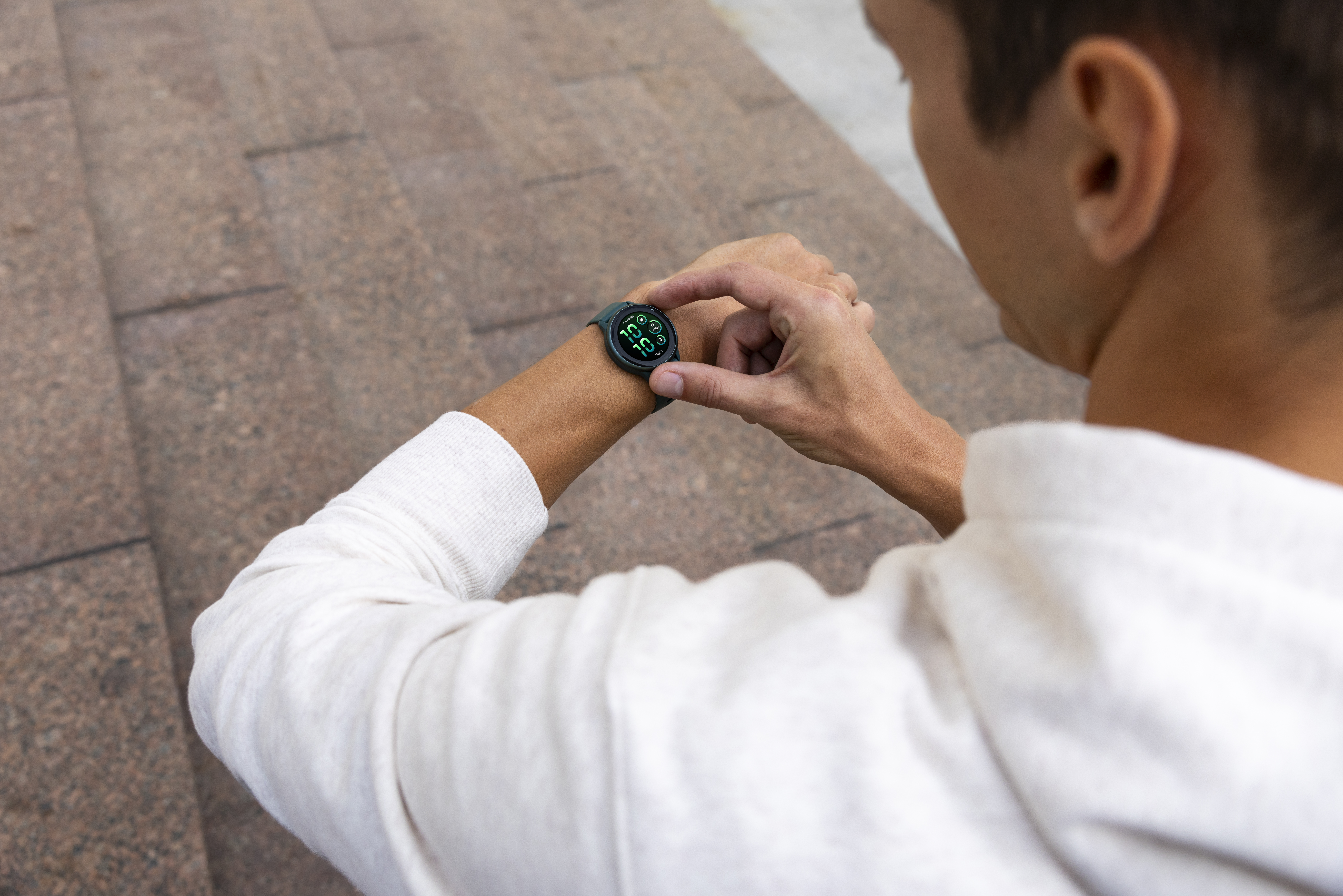 Mann, der auf einer Smartwatch am Handgelenk blickt. Hintergrund: Betonstufen.