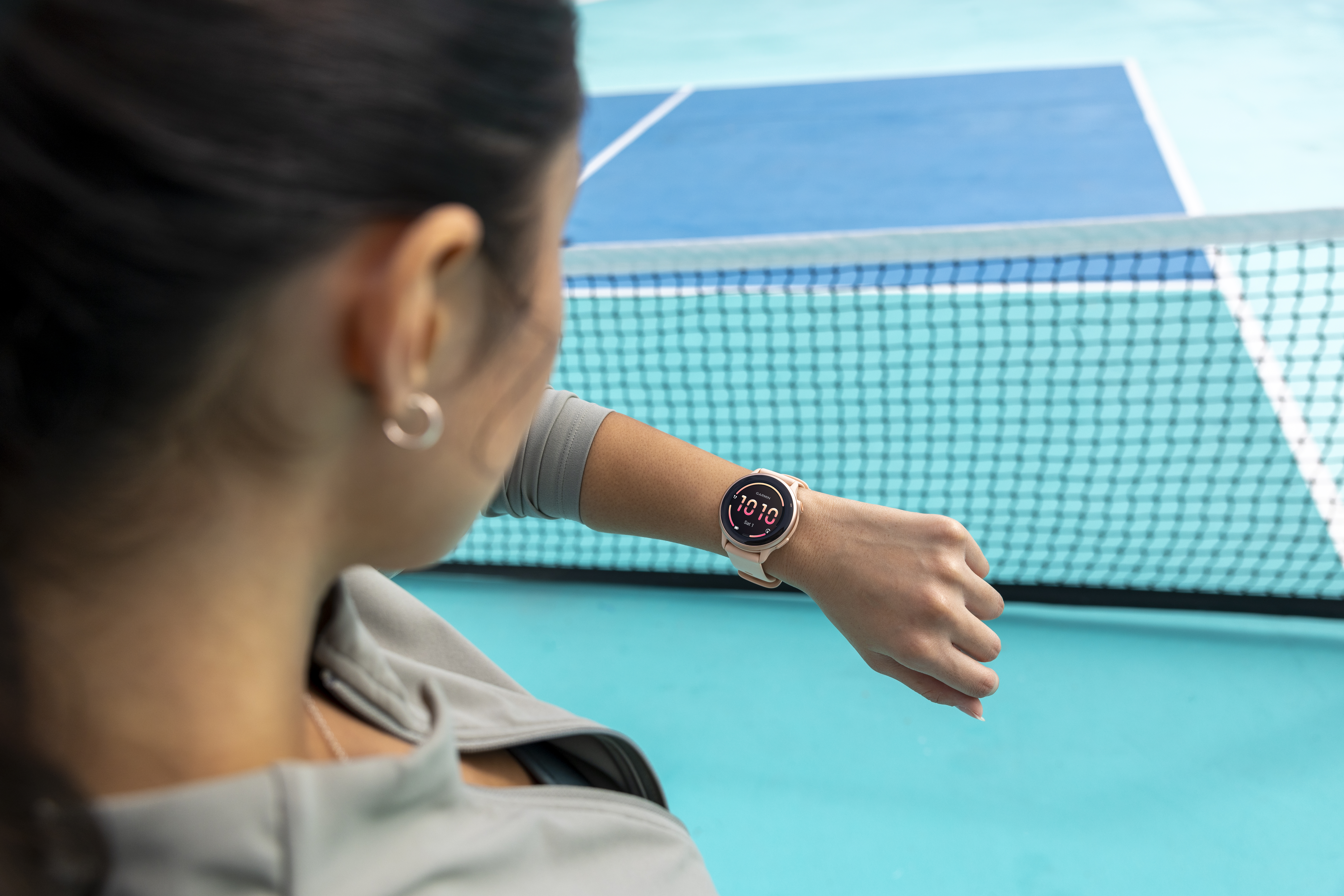 Frau trägt eine Uhr am Handgelenk. Blauer und grüner Tennisplatz im Hintergrund.
