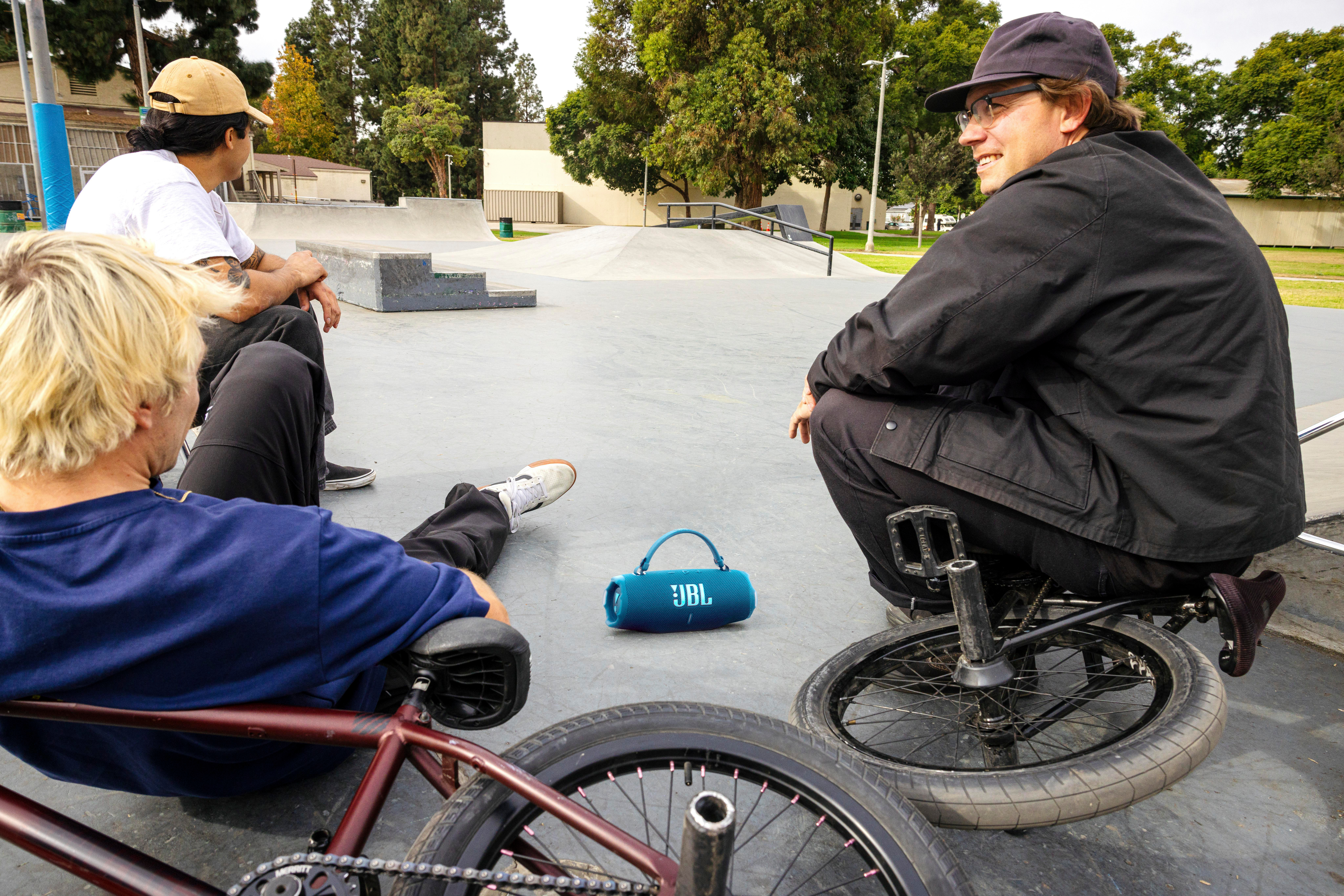 Drei Personen und ein blauer Lautsprecher in einem Skatepark. Eine Person lächelt und schaut die anderen an.