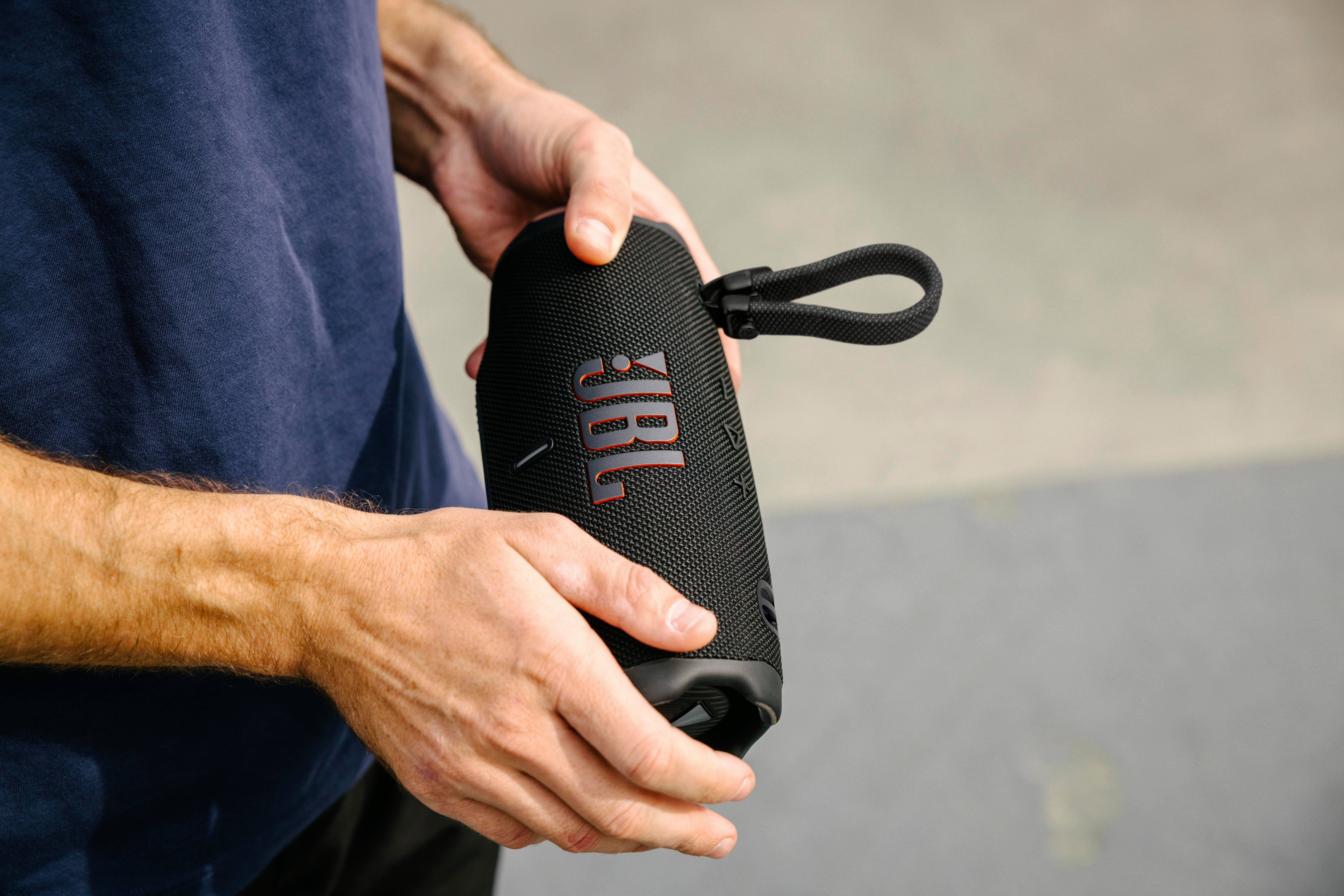 Eine Person hält einen schwarzen JBL-Lautsprecher mit schwarzem Griff.
