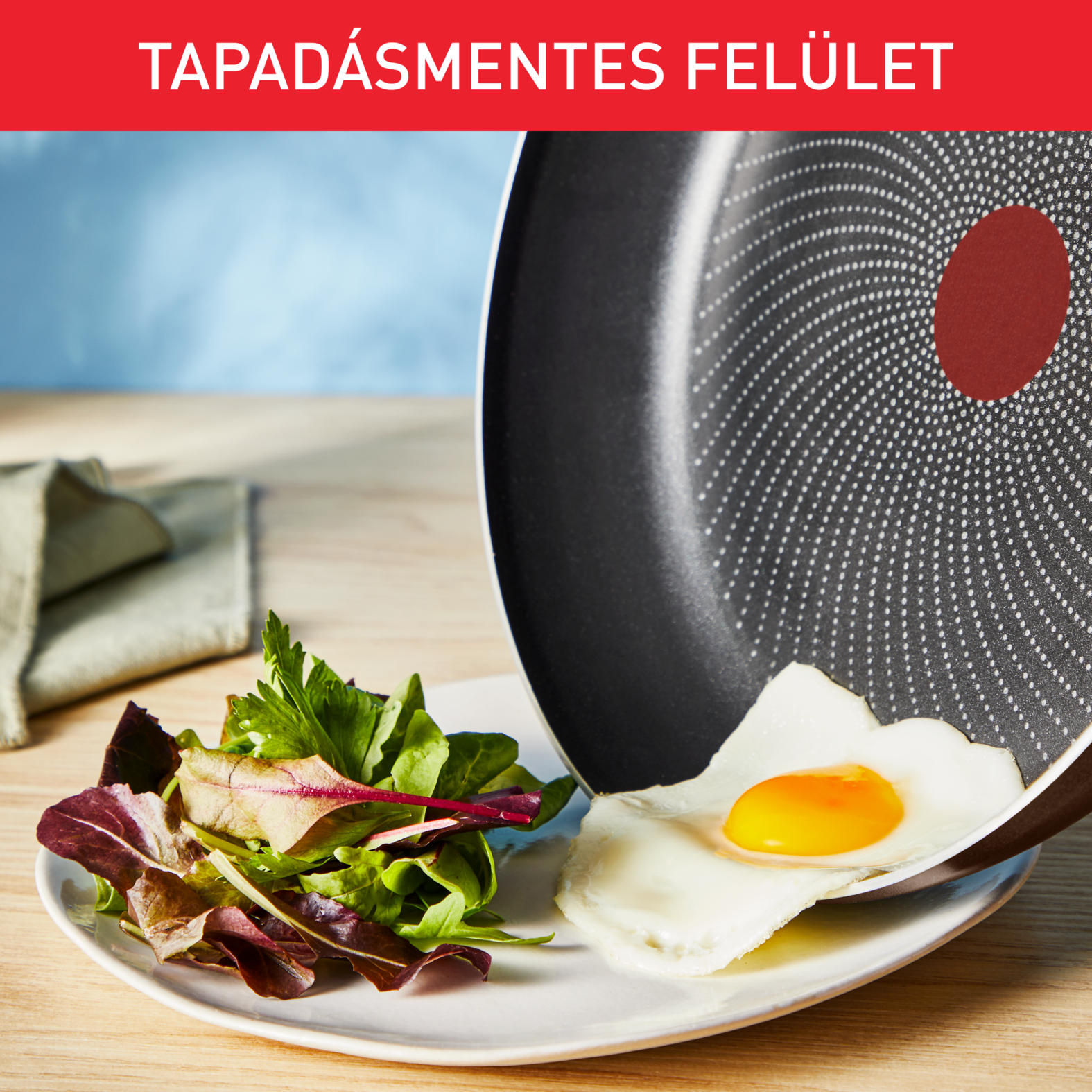 Egy tojást fehér tányérra helyeznek, saláta mellett. A serpenyő fekete, a tányér fehér.